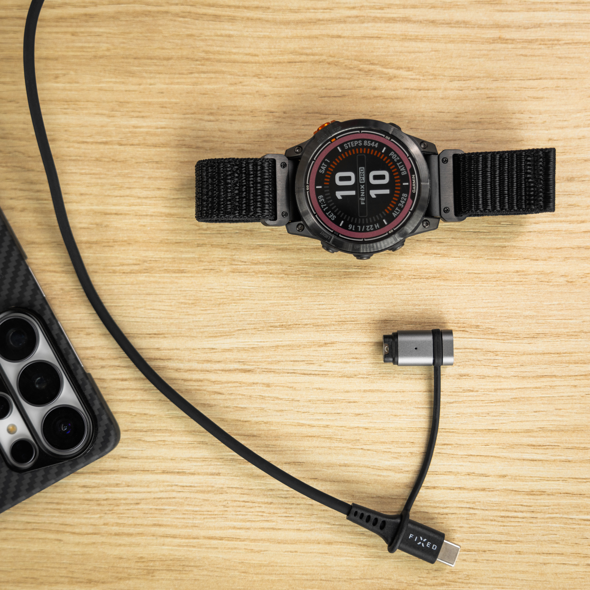 Smartwatch, Handyhülle und Ladekabel liegen auf Holz.