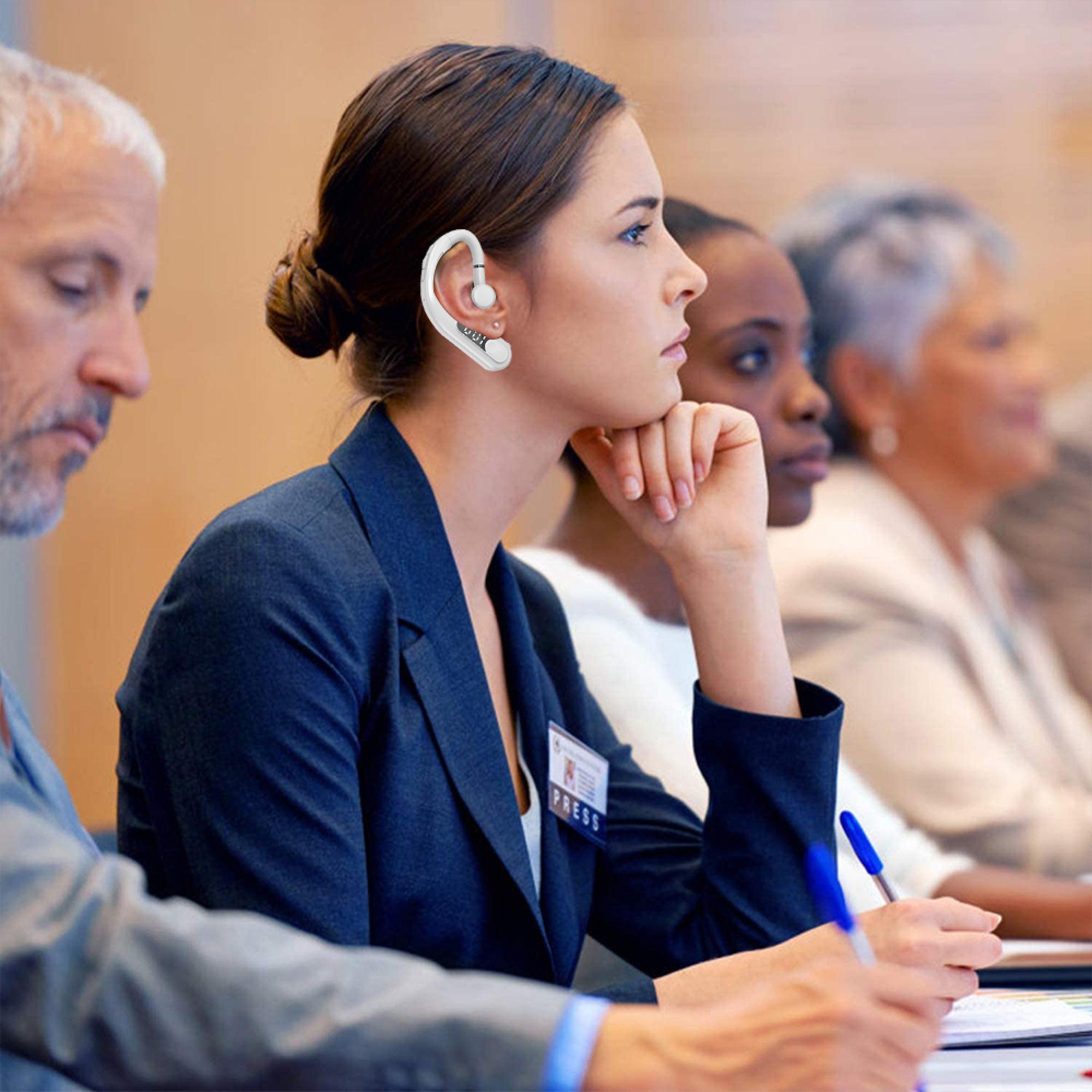 Frauen und Männer sitzen in einem Konferenzraum, eine Frau trägt ein Headset.