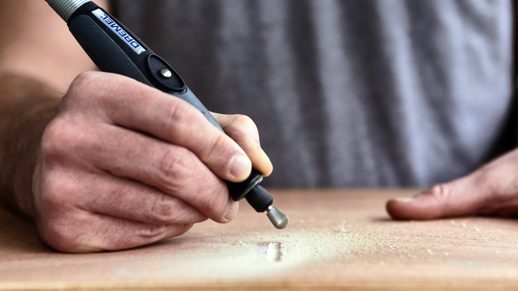 Hand hält Dremel-Werkzeug und graviert Holz. Holzspäne fliegen.