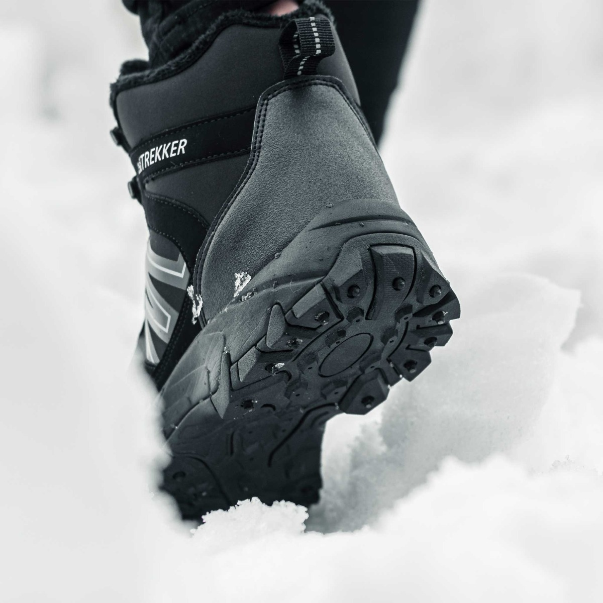 Ein schwarzer TREKKER-Stiefel mit dicker Sohle tritt durch weißen Schnee.