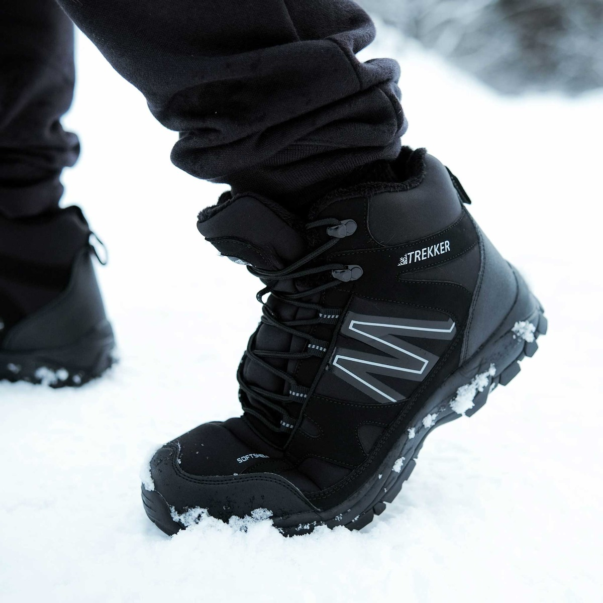 Schwarzer Winterstiefel mit Schnürsenkeln und dem Logo „TREKKER“ auf Schnee.