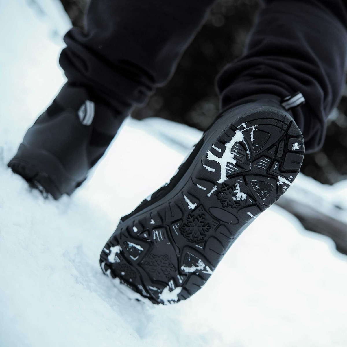 Nahaufnahme von schwarzen Stiefeln, die im Schnee gehen, mit Schnee auf der Sohle.