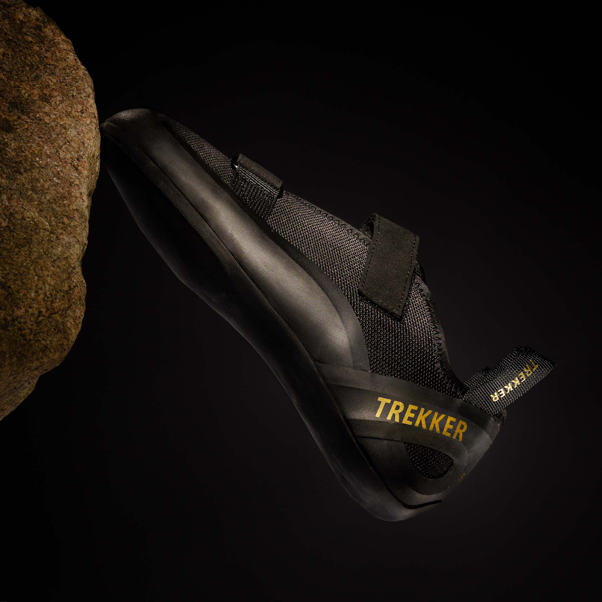 Ein schwarzer Kletterschuh mit gelbem Aufdruck 'TREKKER' auf einem Felsen.