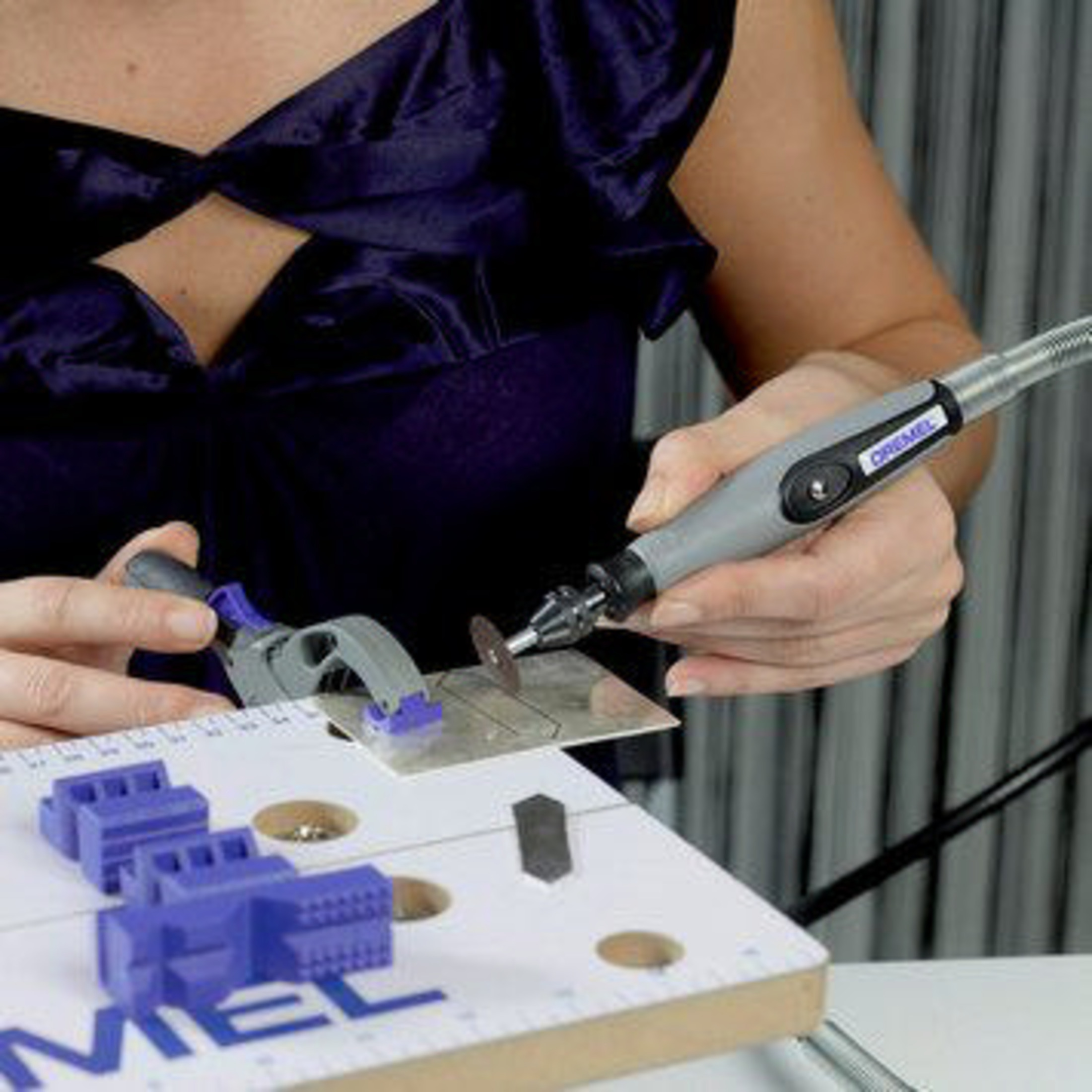 Nahaufnahme einer Person, die mit einem Dremel-Werkzeug Metall auf einer Werkbank mit Klemmen schneidet.