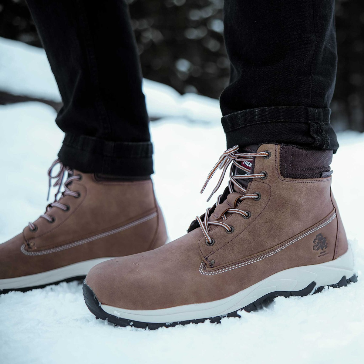 Braune Lederstiefel mit weißen Sohlen und Schnürsenkeln stehen im Schnee.