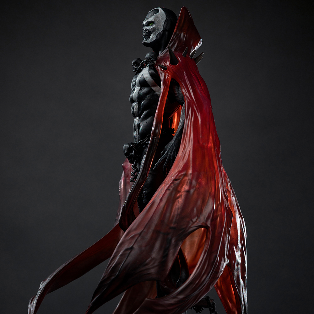 Una figura scura con mantello rosso e volto bianco, che guarda a sinistra.