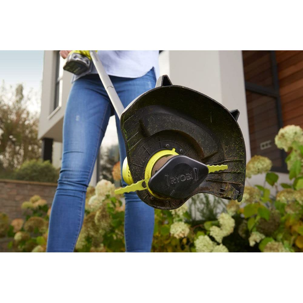 Eine Person in Jeans hält einen Rasentrimmer mit gelbem Akku und schwarzem Schutz.