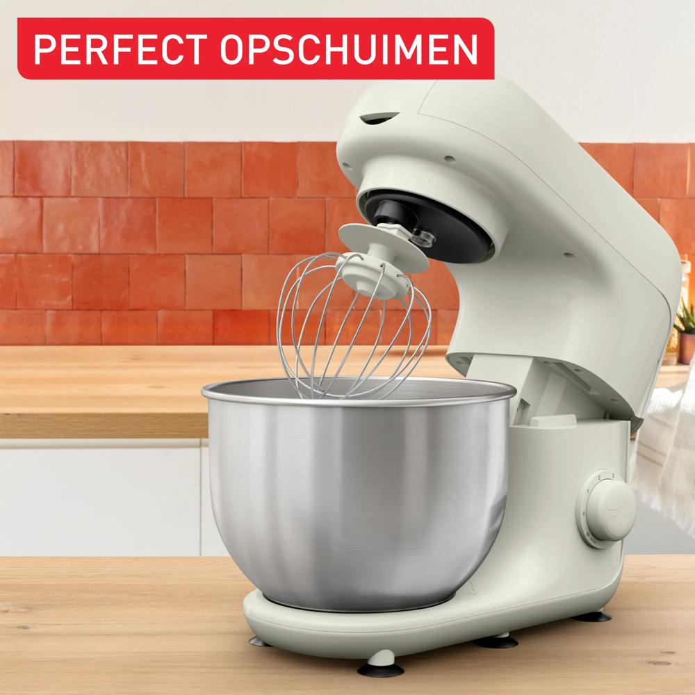 Ein cremefarbener Standmixer mit Schneebesen und Edelstahlschüssel auf einem Holztisch.