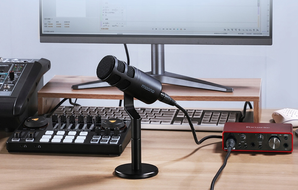 Un microfono Maono è su un supporto davanti a un monitor del computer e attrezzatura audio.