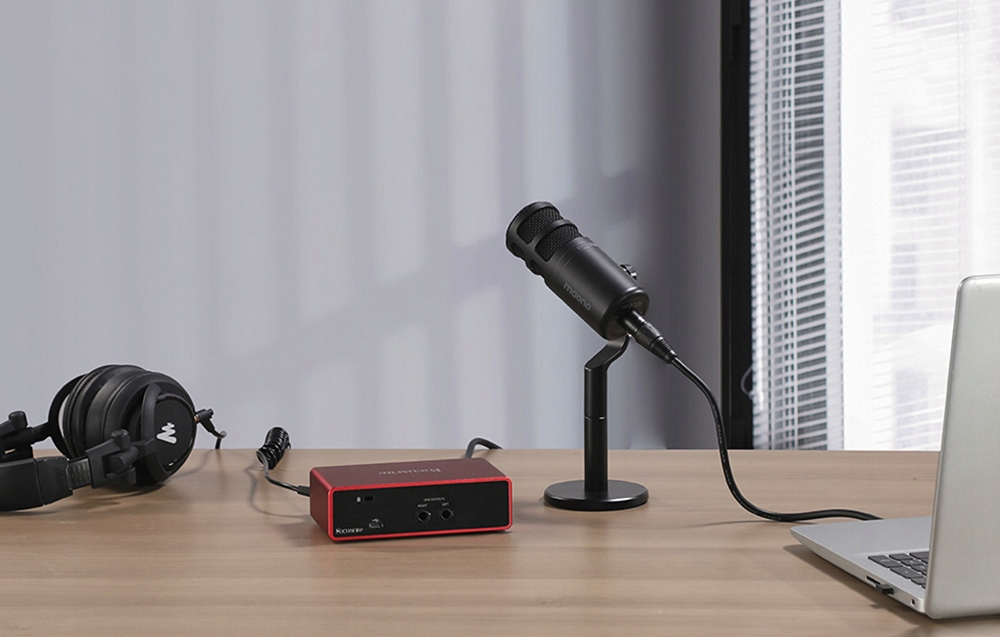 Un microfono nero, cuffie e un'interfaccia audio rossa su un tavolo di legno.