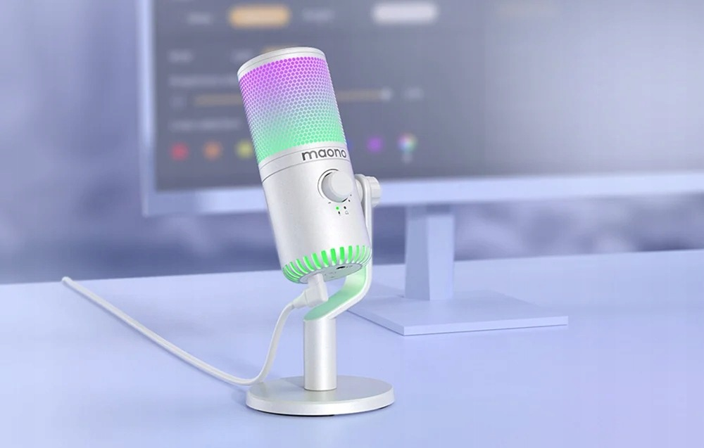 Ein weißes Mikrofon mit RGB-Licht auf einem Schreibtisch, im Hintergrund ein Monitor.
