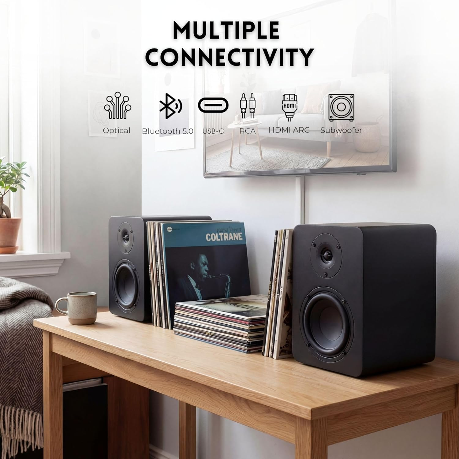 Dos altavoces negros sobre una mesa de madera, con discos y una taza al lado.
