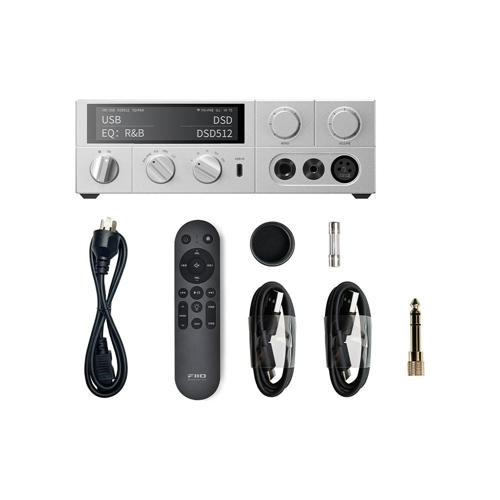 Srebrne urządzenie audio z kablami, pilotem i adapterem na białym tle.