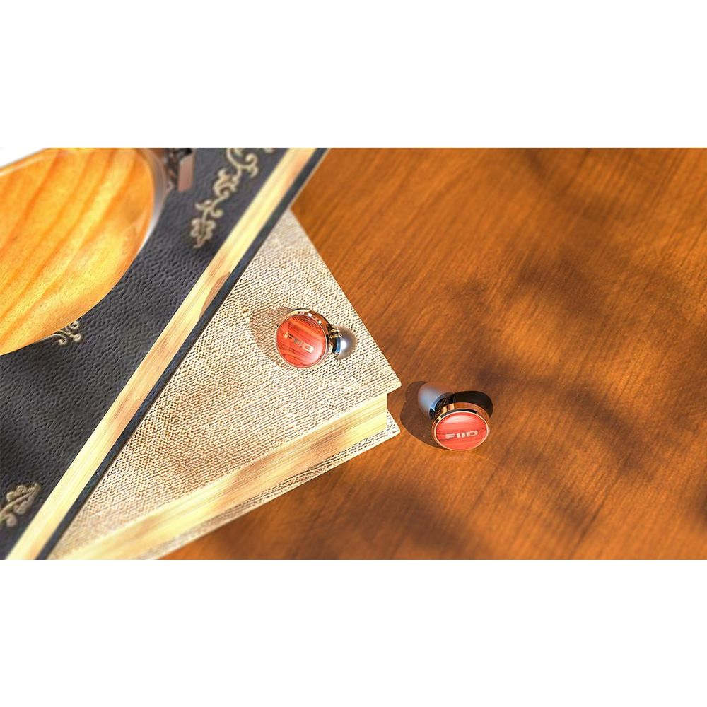 Dos auriculares rojos con detalles dorados sobre una superficie de madera junto a un libro.