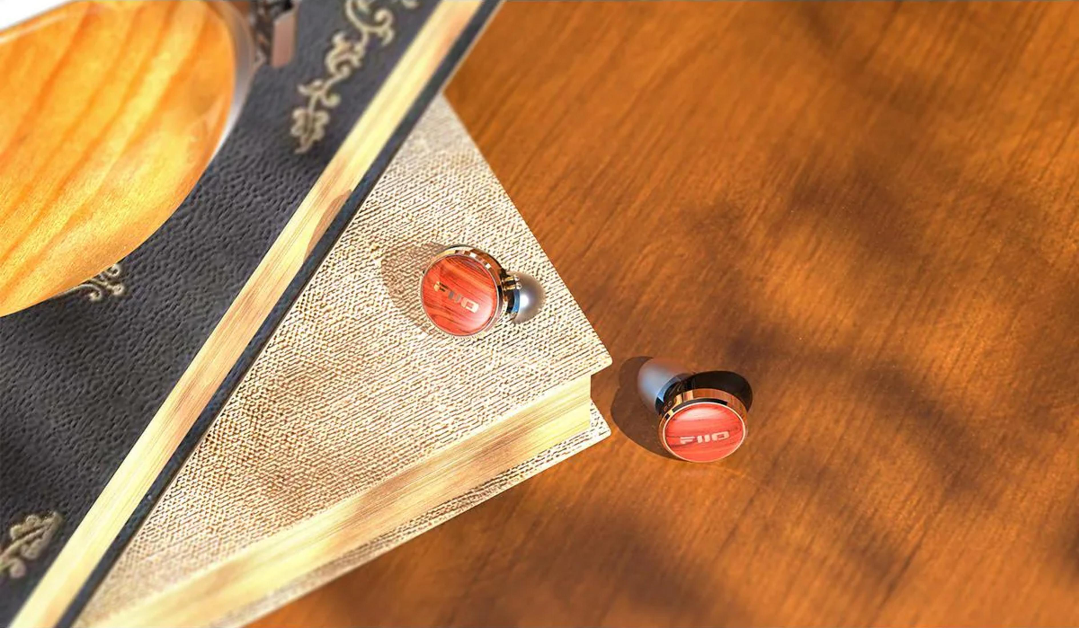 Dos auriculares rojos de madera descansan sobre una mesa de madera junto a un libro.