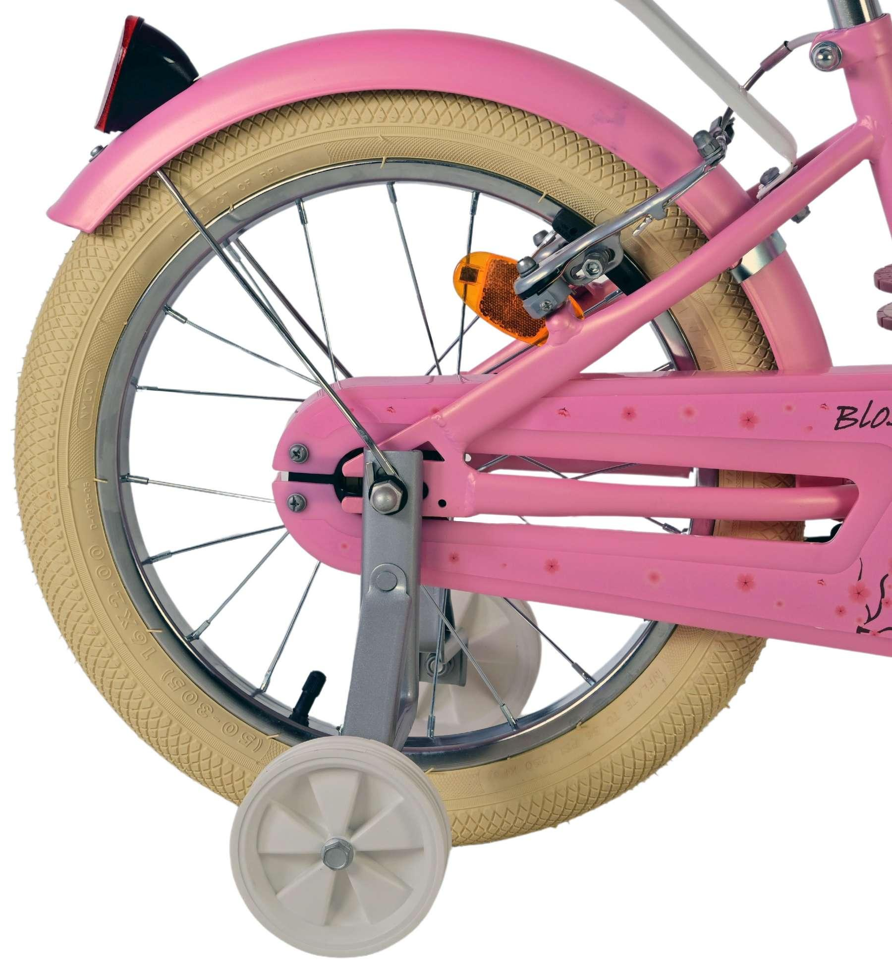 Nahaufnahme eines rosa Kinderfahrrads mit Stützrädern, beigem Reifen und rotem Rücklicht.