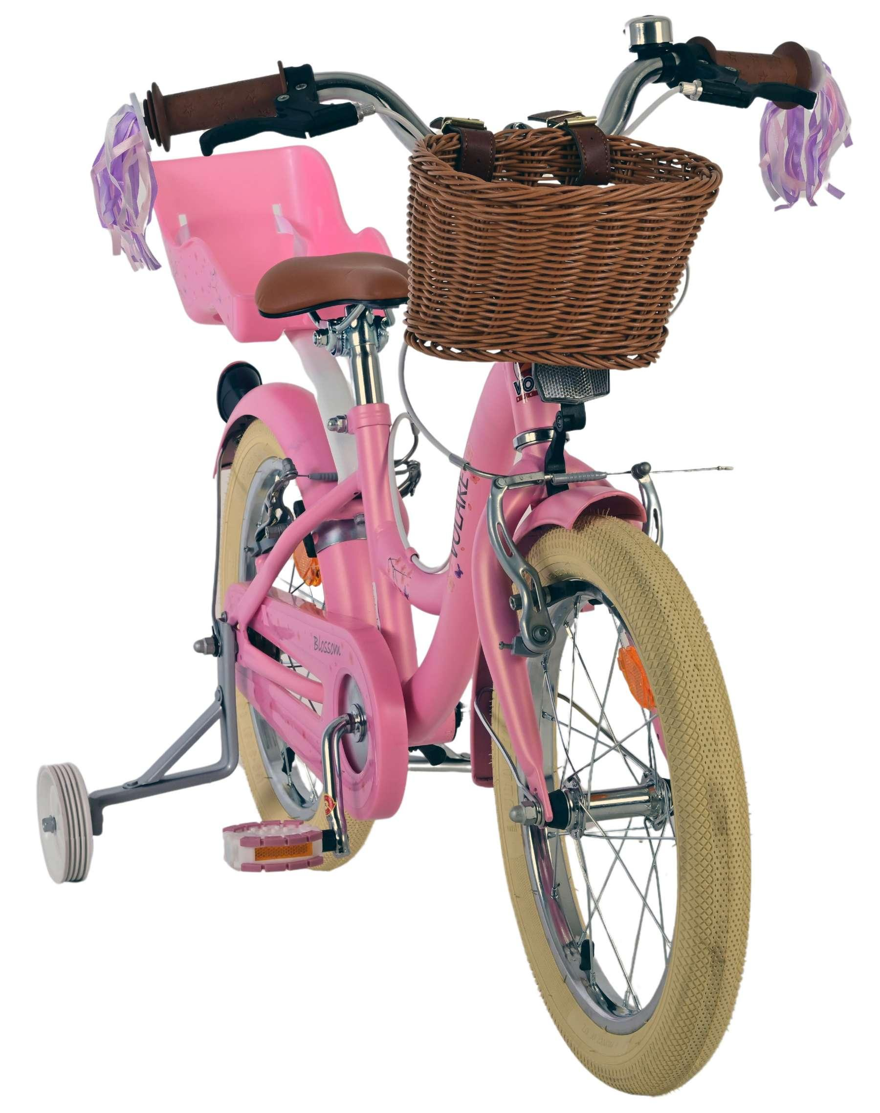Ein rosafarbenes Kinderfahrrad mit Stützrädern, braunem Sattel und Korb.