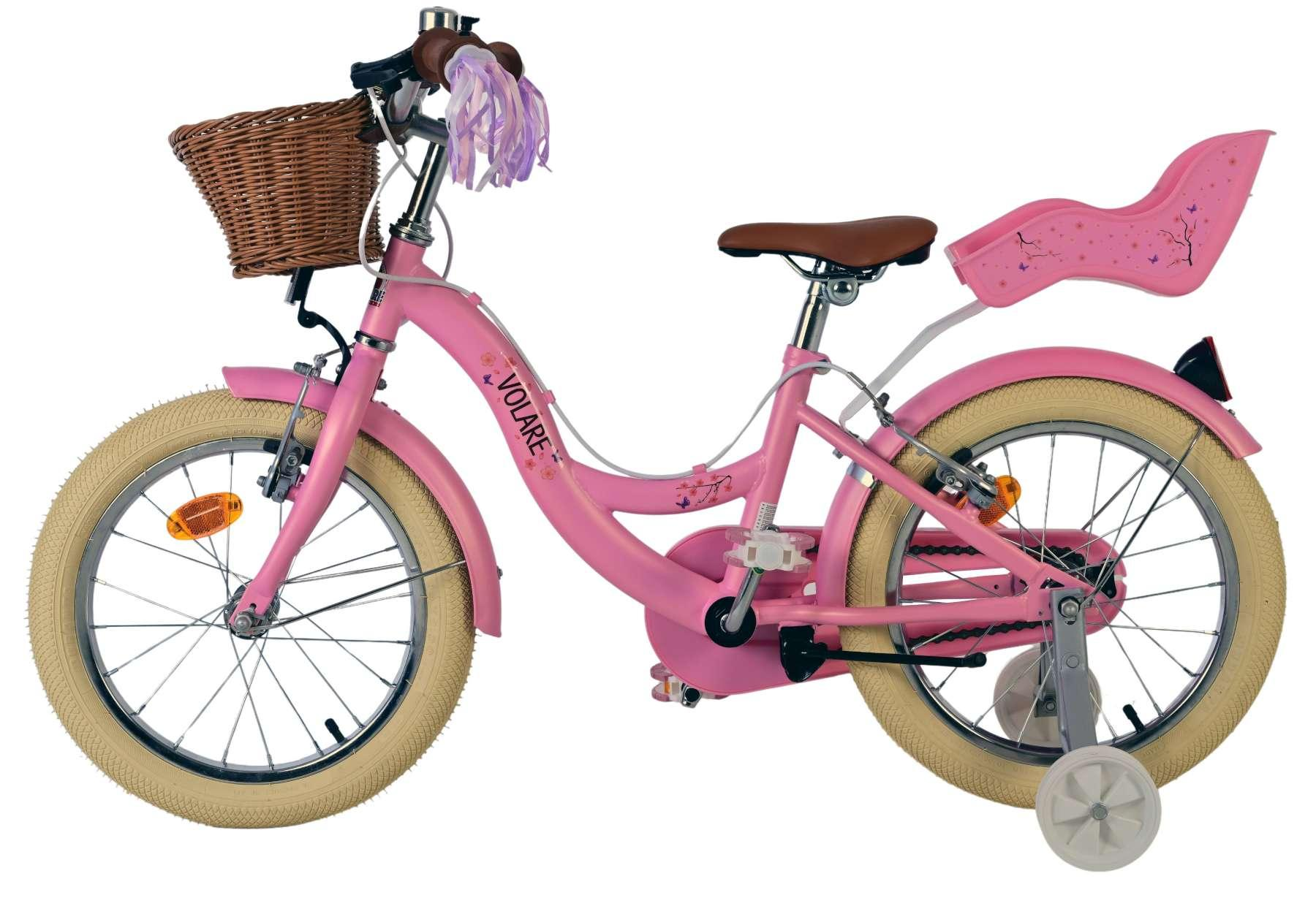 Ein pinkes Kinderfahrrad mit braunem Sattel, Weidenkorb und rosa Puppentrage, vor weißem Hintergrund.
