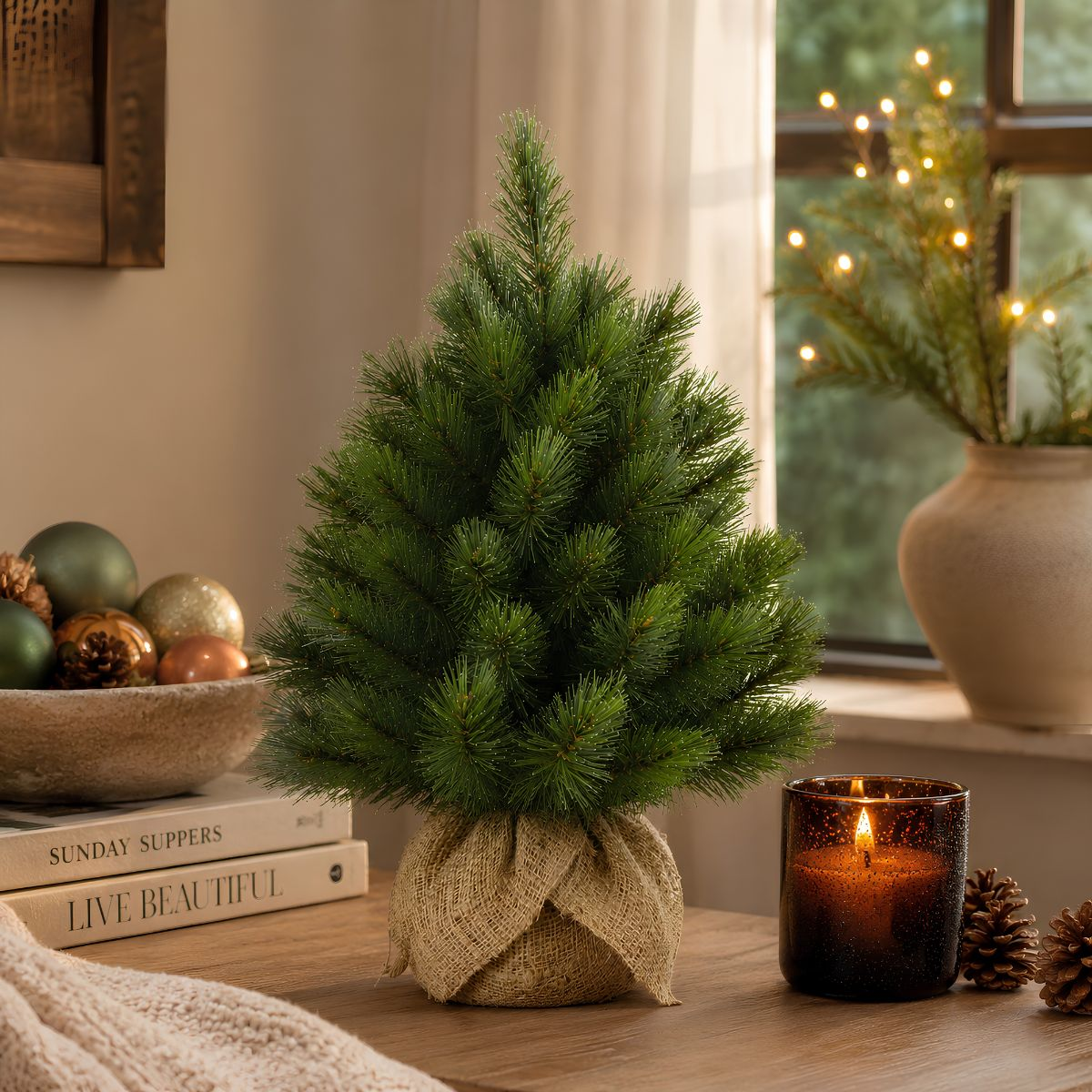 Small Christmas tree in burlap, with candle, pinecones, and ornaments.