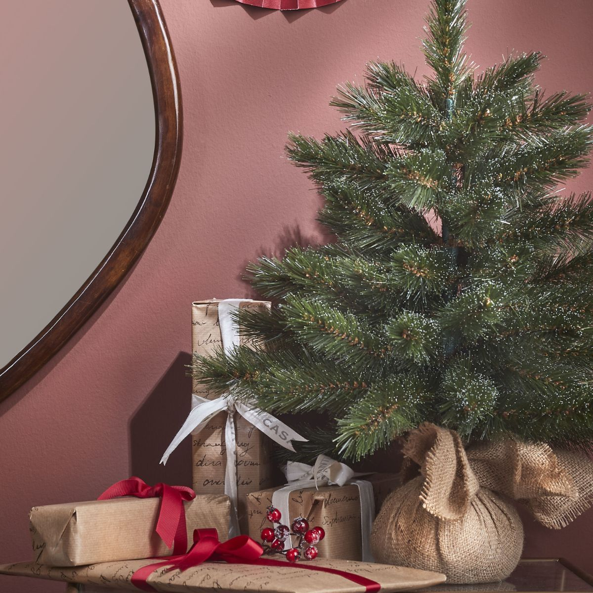 Un petit sapin de Noël avec des cadeaux et un miroir en arrière-plan.
