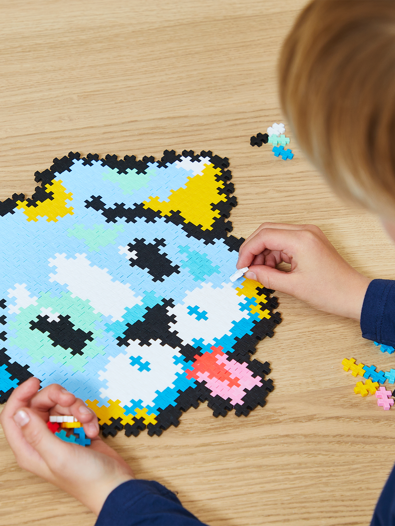 Ein Kind baut ein buntes Mosaik aus kleinen Plastiksteinen auf einem Holztisch.
