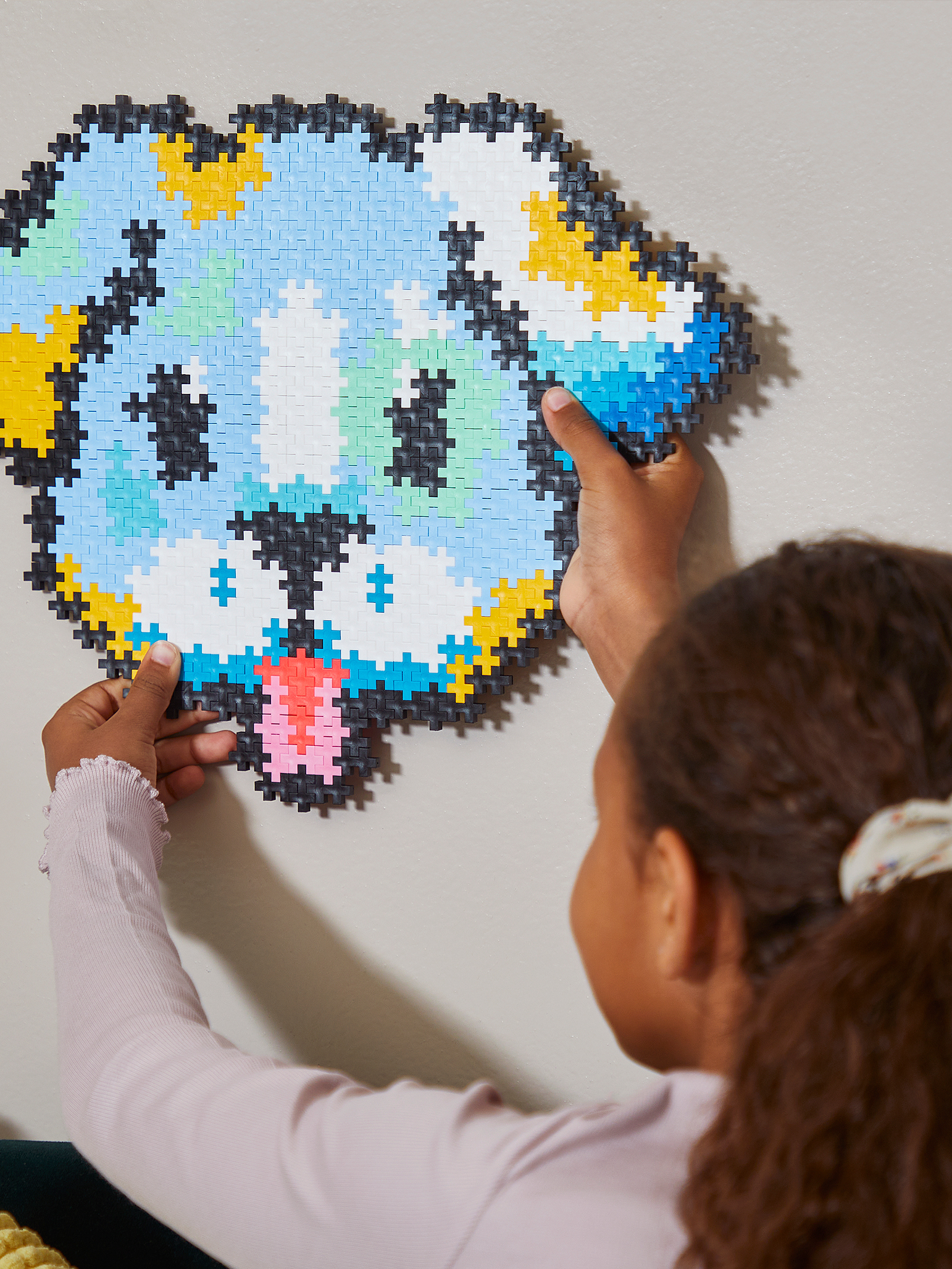 Ein Kind hält ein buntes, aus Steckbausteinen gefertigtes Hunde-Mosaik an eine Wand.