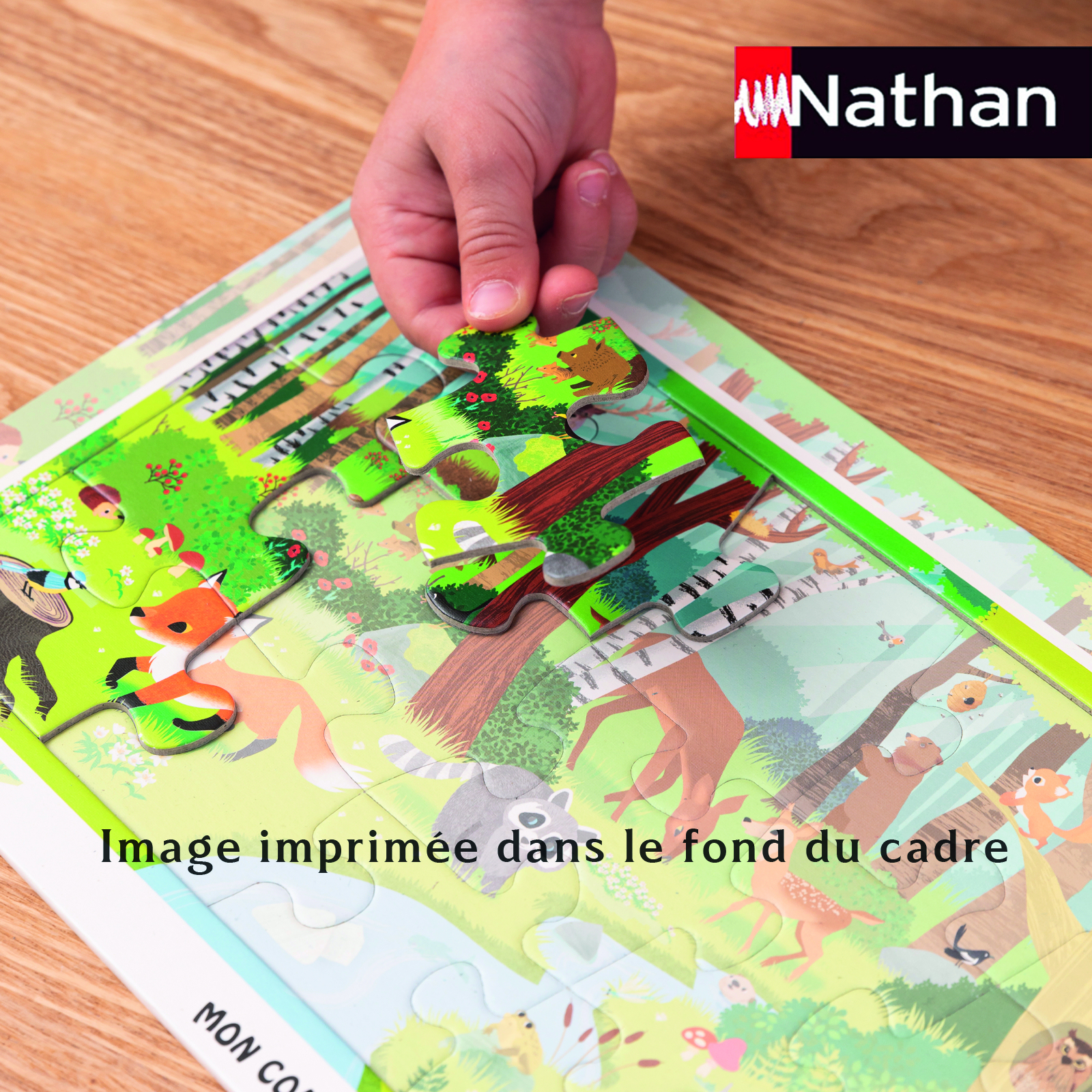 Ein Kind legt ein Puzzleteil mit einem Bären auf ein Waldpuzzle mit Tieren.