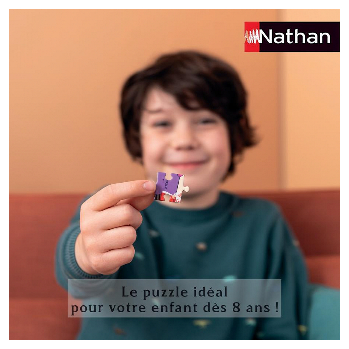 Ein Junge hält ein kleines Puzzleteil mit einer lila Figur. Nathan-Logo oben.
