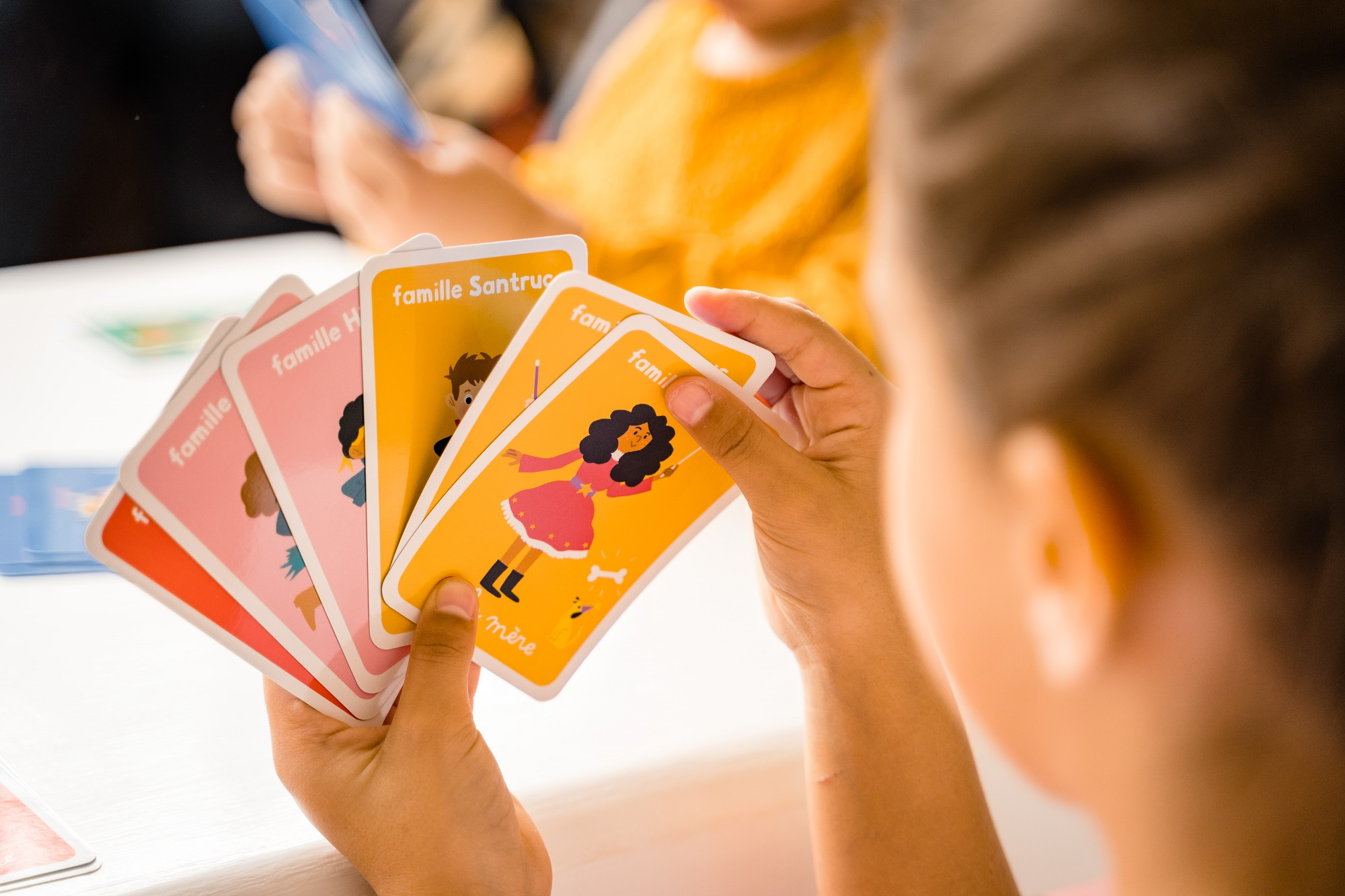Hände halten Spielkarten mit bunten Illustrationen von Familienmitgliedern.