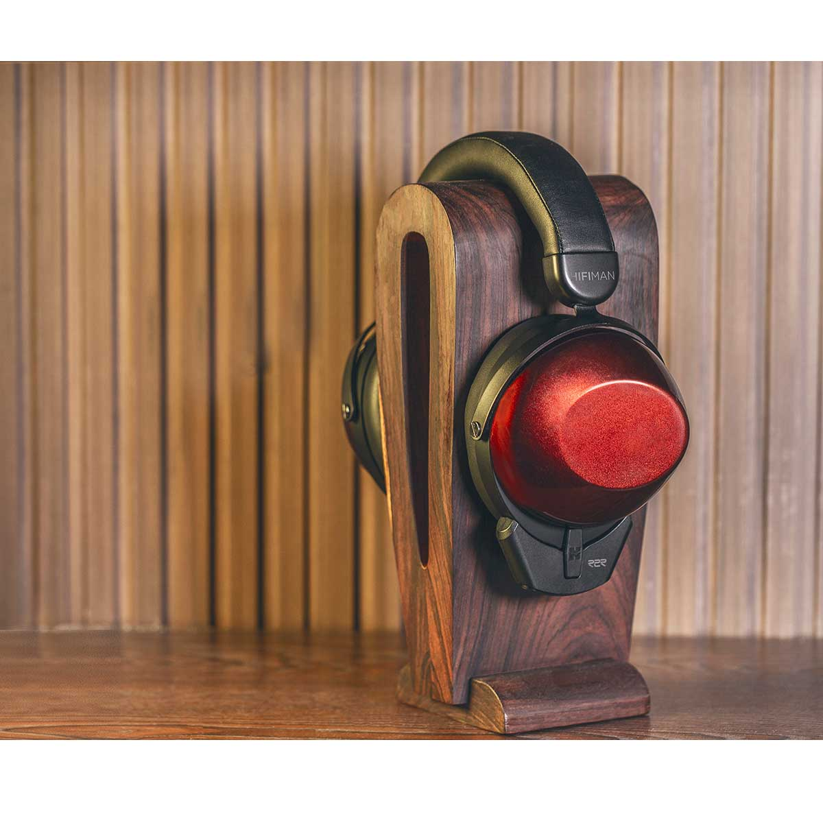 Auriculares con copas rojas en un soporte de madera frente a una pared de madera.