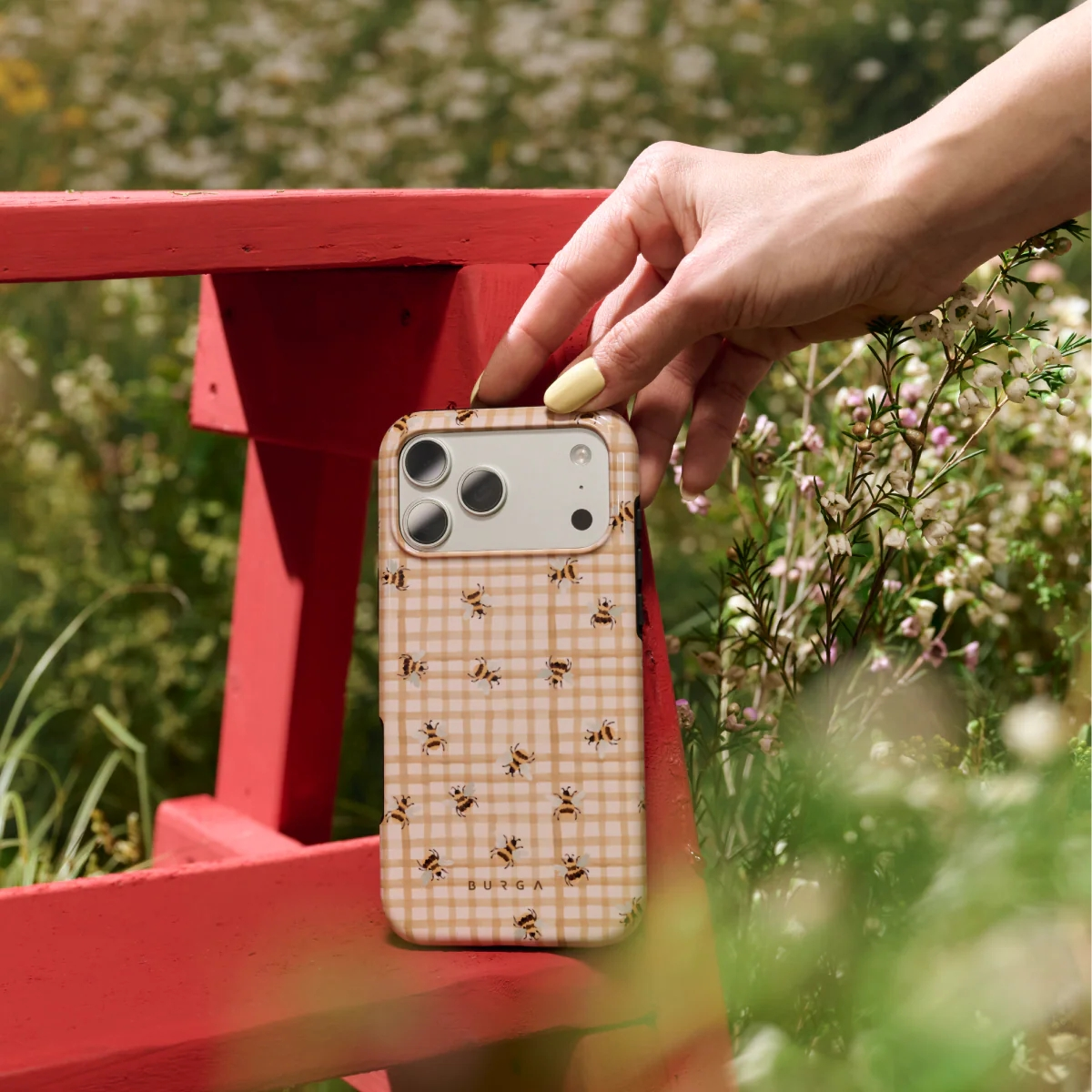 A hand holds a phone with a bee pattern on a beige checkered case outdoors.
