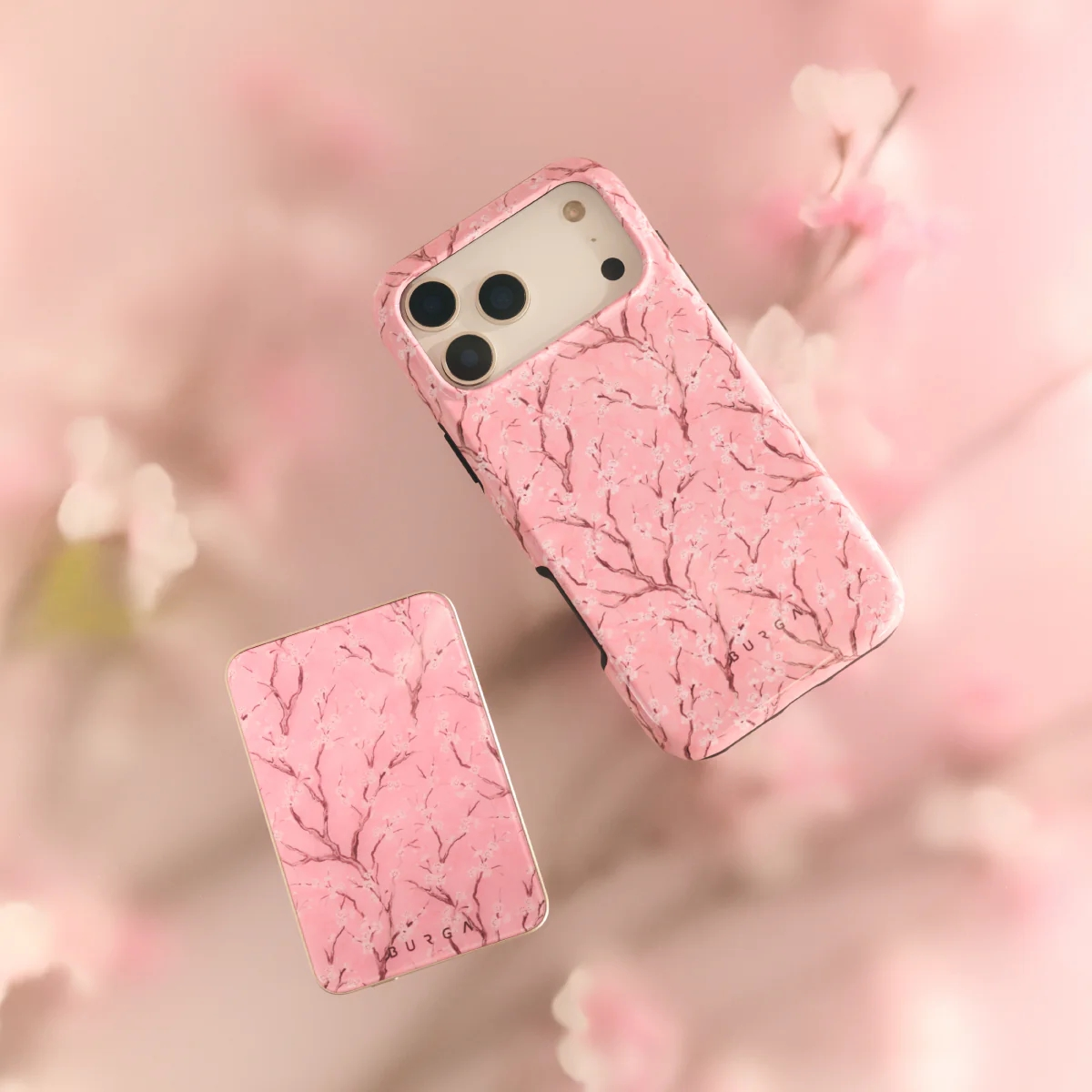 Roze iPhone hoesje en powerbank met kersenbloesem design op roze achtergrond.