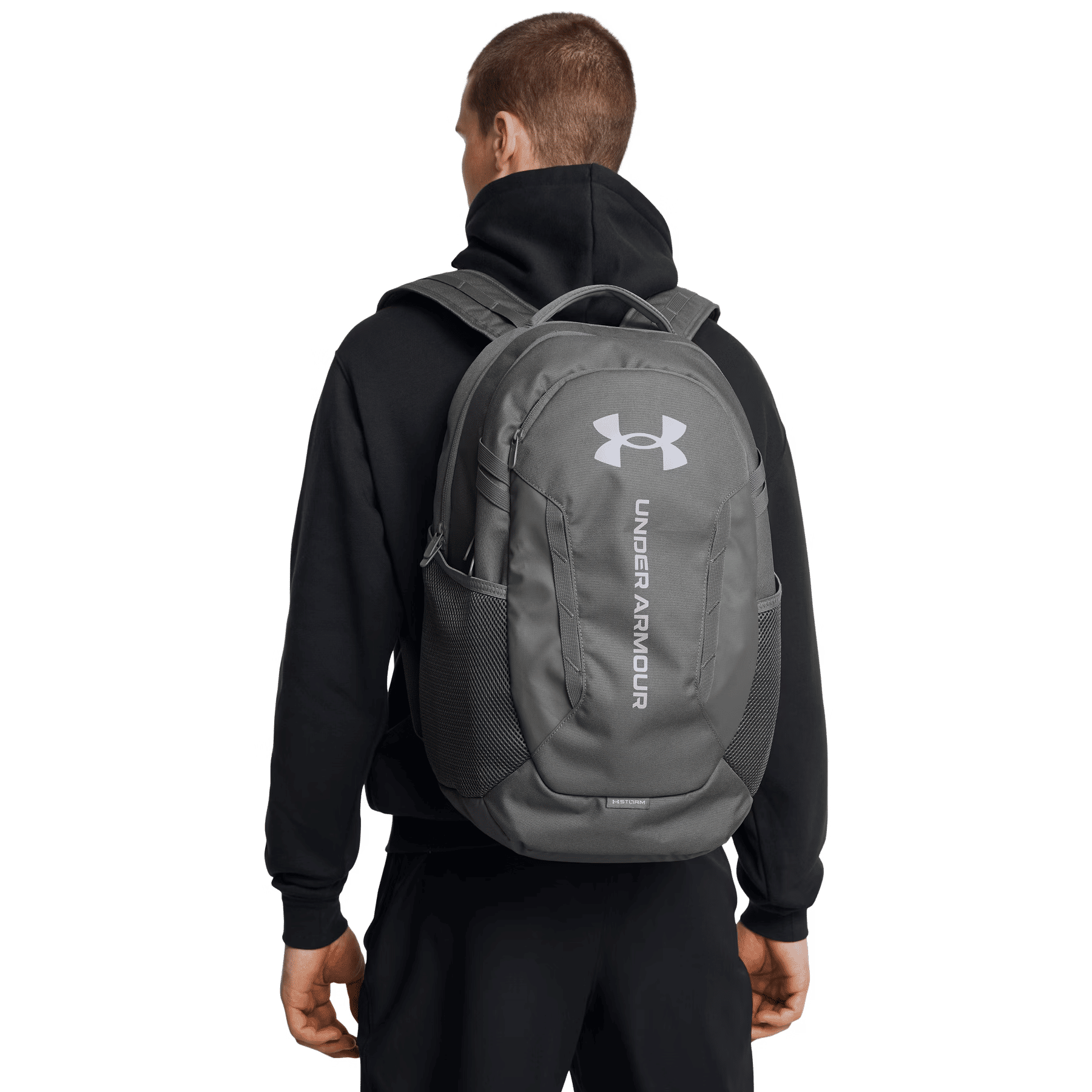 Mann trägt einen grauen Under Armour Rucksack und schwarze Kapuzenjacke. Weißes Logo.