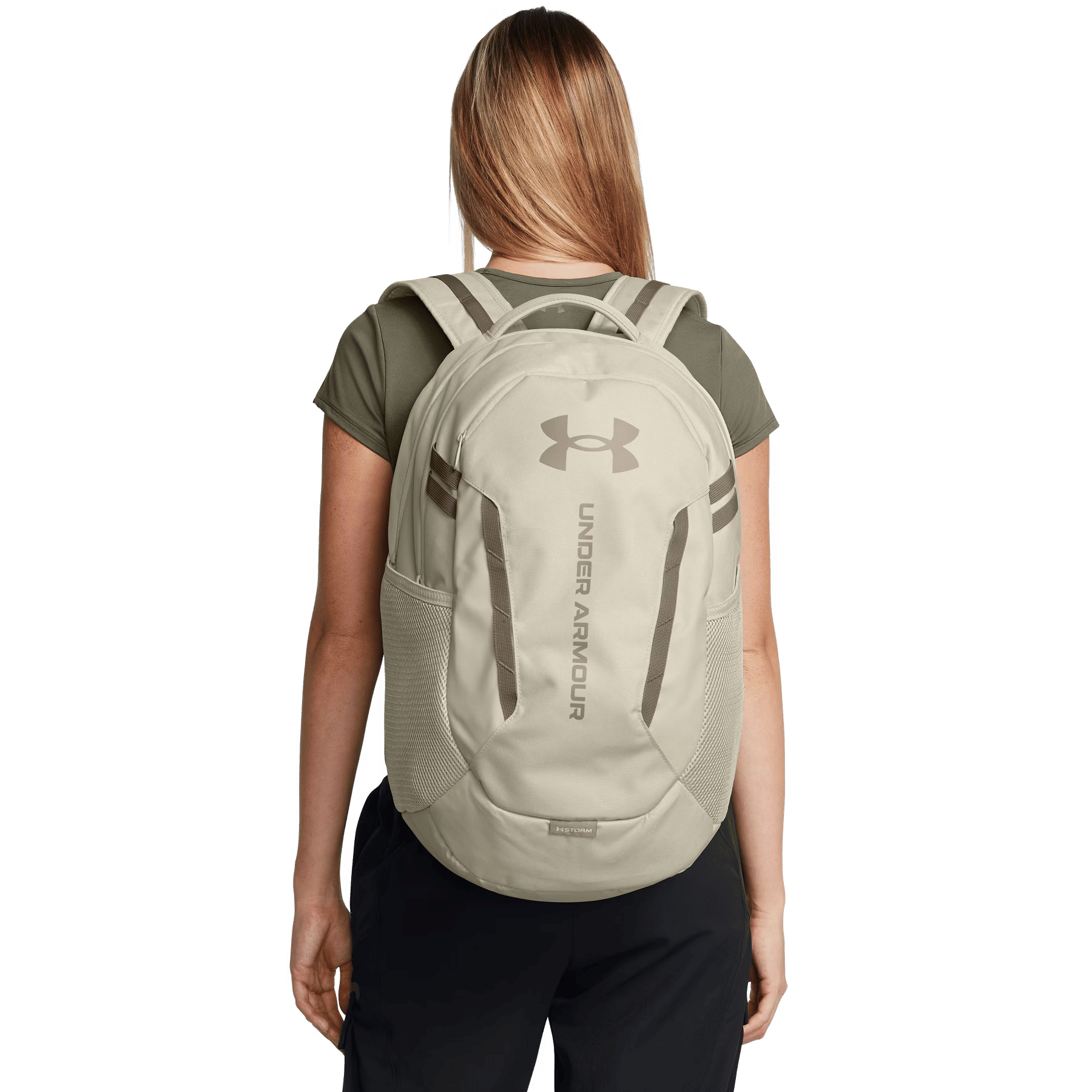 Eine Frau mit blonden Haaren trägt einen beigefarbenen Rucksack mit dem Under Armour Logo.