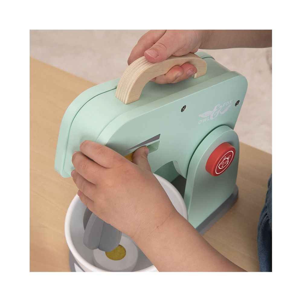 Kinderhände bedienen einen mintgrünen Spielzeugmixer mit Holzgriff.