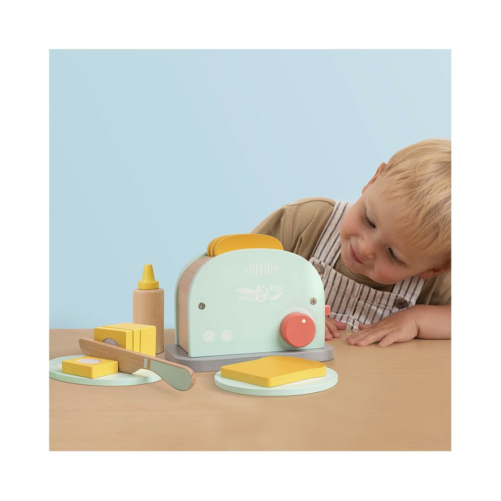 Ein kleiner Junge spielt mit einem Holzspielzeug-Toaster, Toast und Butter.