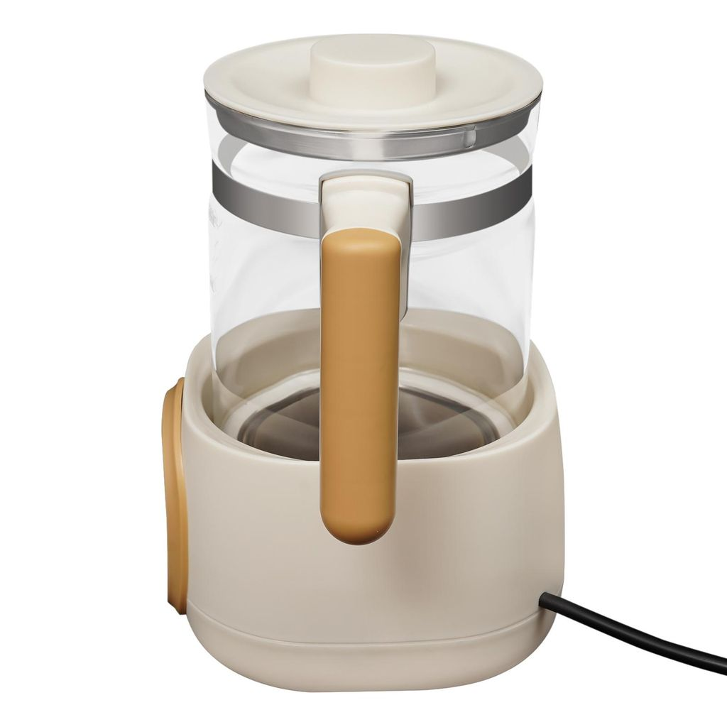 Eine cremefarbene Teekanne aus Glas mit braunem Griff auf einer Basis mit schwarzem Kabel.