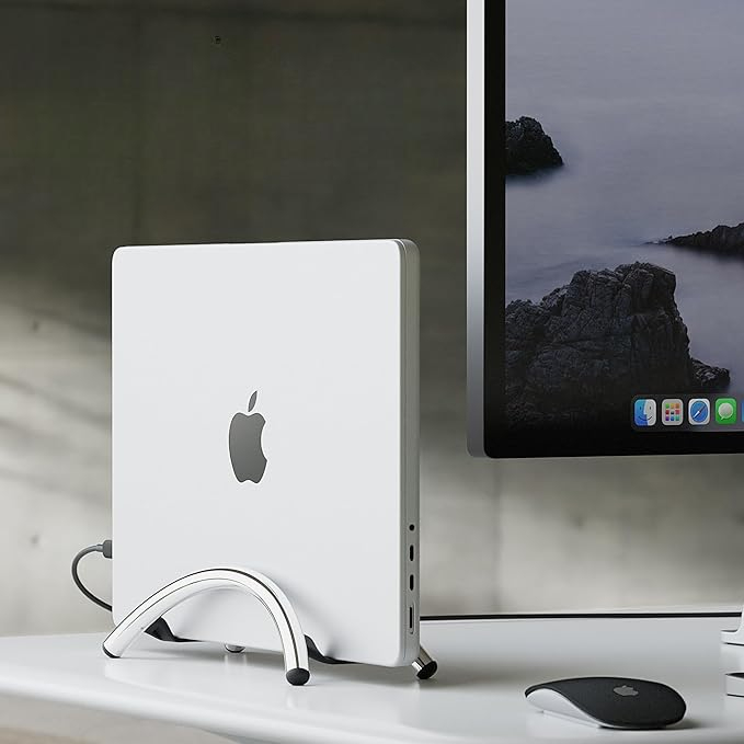 A white Apple Mac Mini stands on a desk next to a monitor showing rocks.