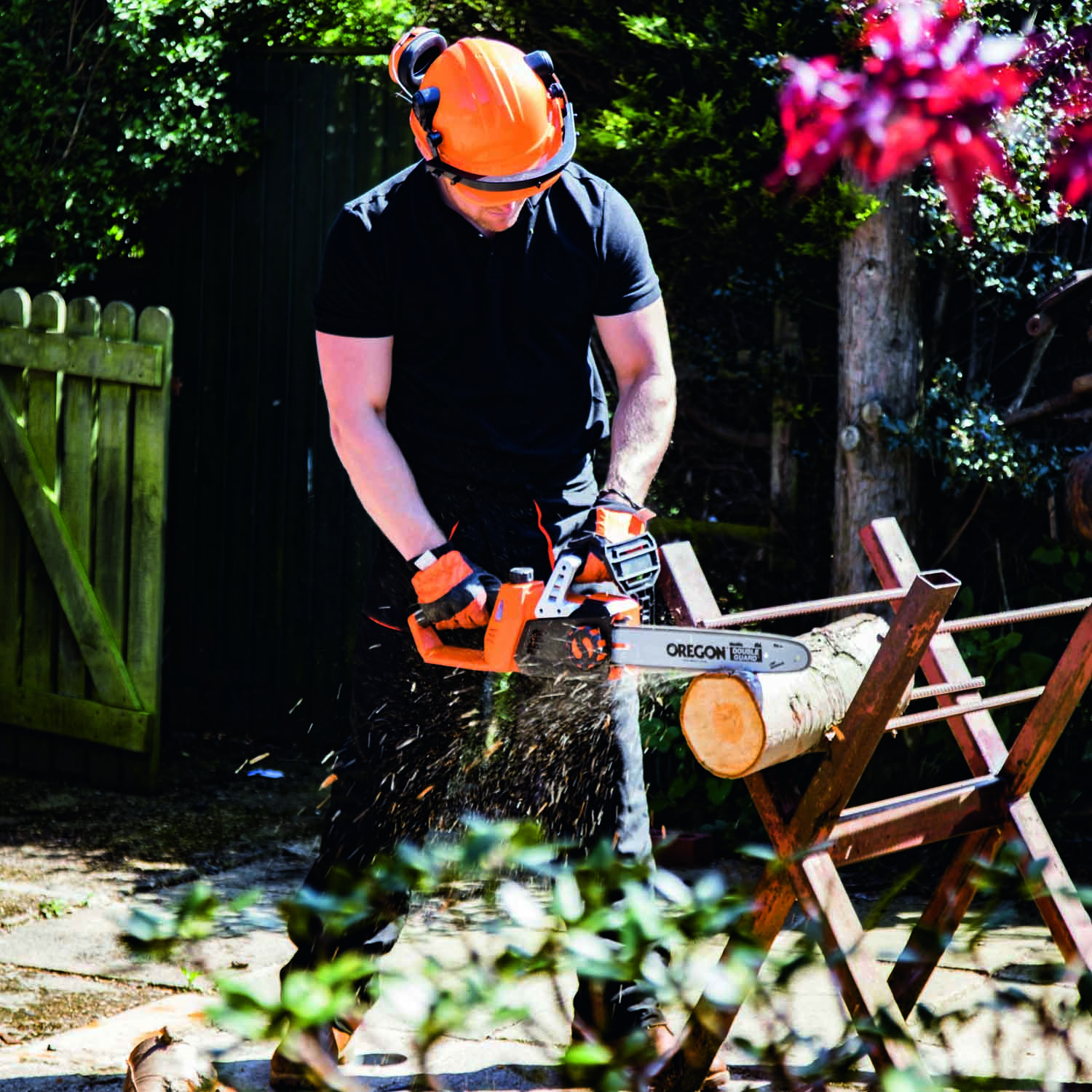 Mann in Schutzkleidung sägt Baumstamm mit Kettensäge im Garten.