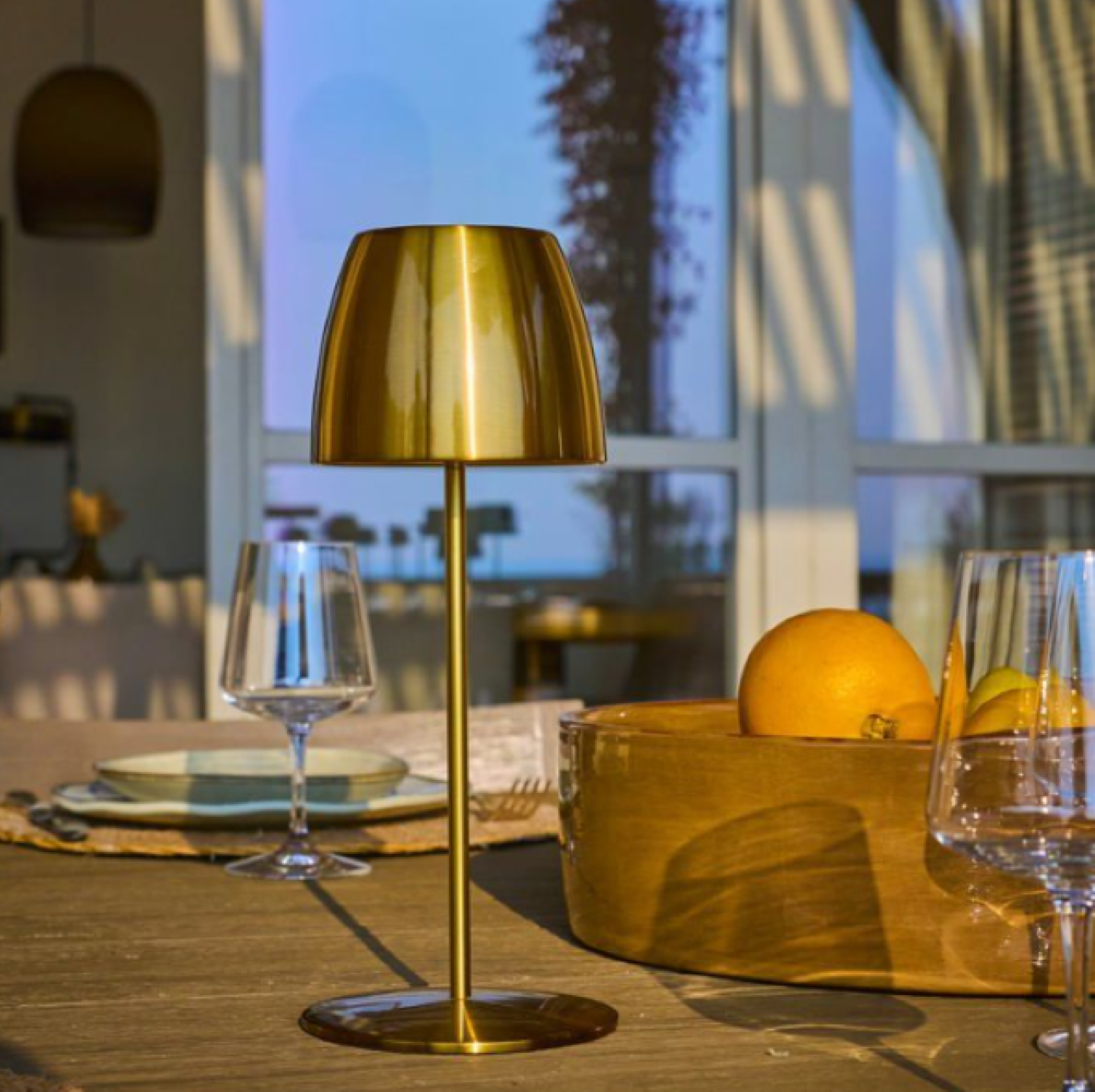 Eine goldene Lampe steht auf einem Holztisch mit Obst und Gläsern.