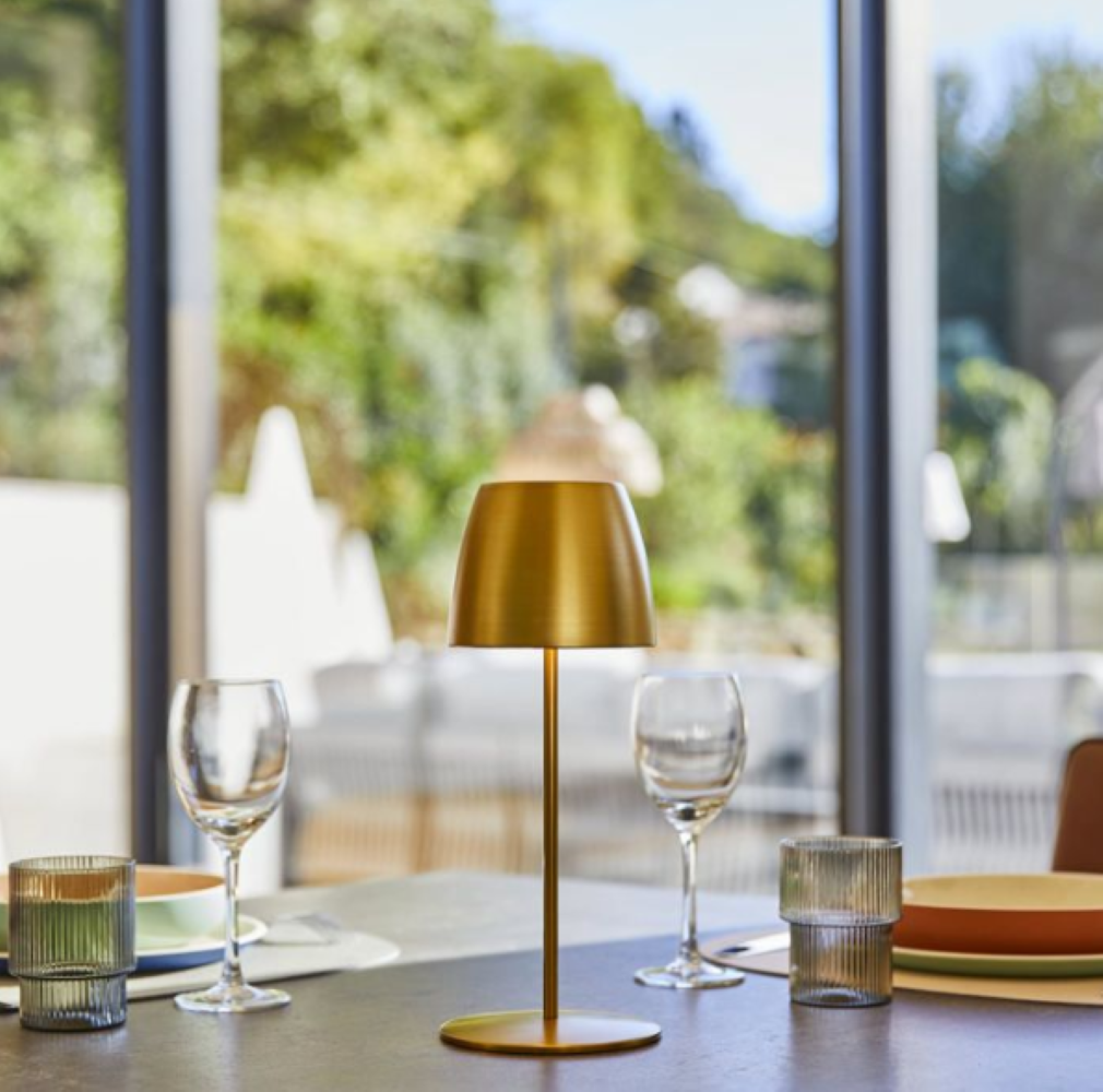 Ein goldener Tischlampen-Mittelpunkt auf einem gedeckten Tisch mit Gläsern und Tellern.