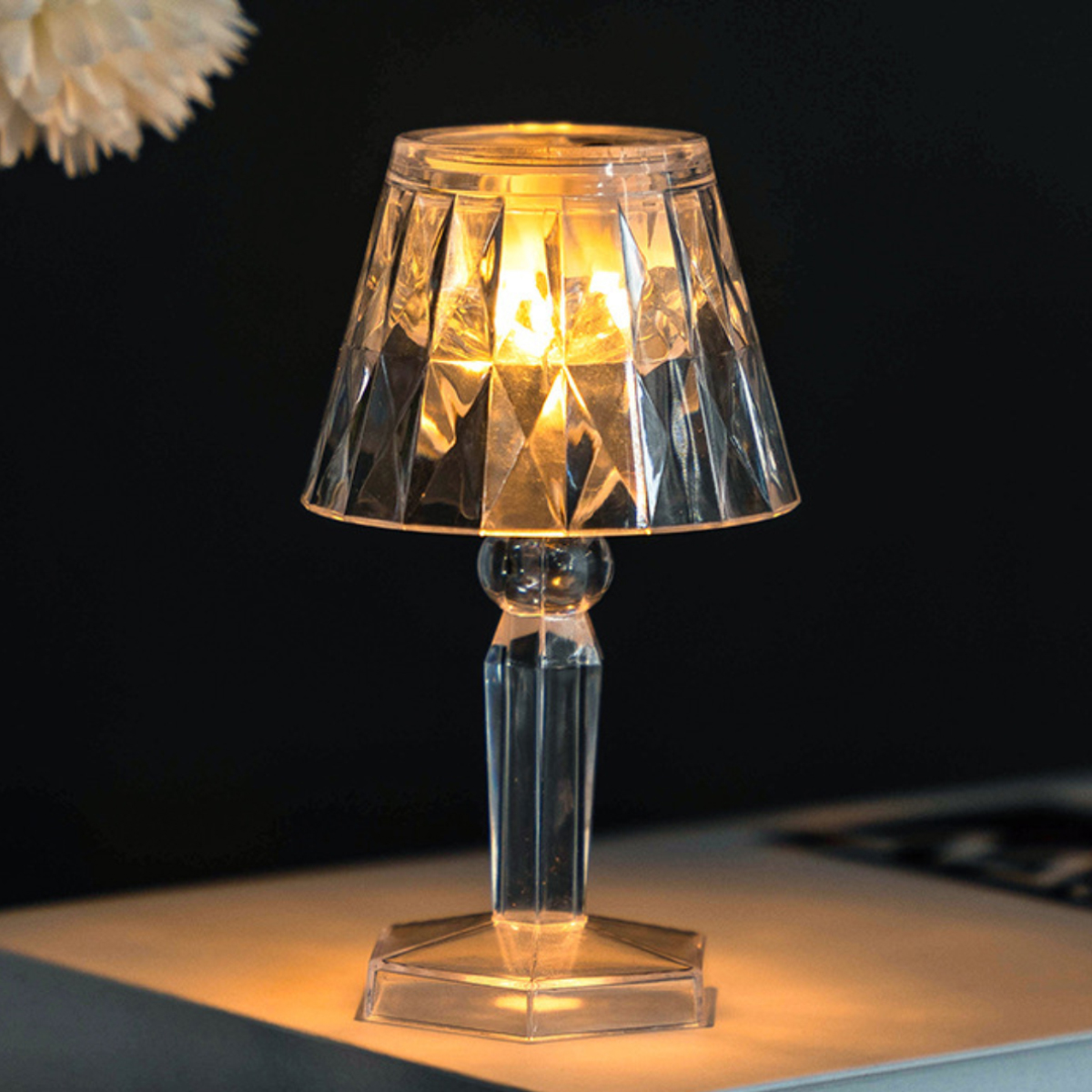 Eine durchsichtige Lampe mit Facettenschliff und warmem Licht auf einem Tisch.