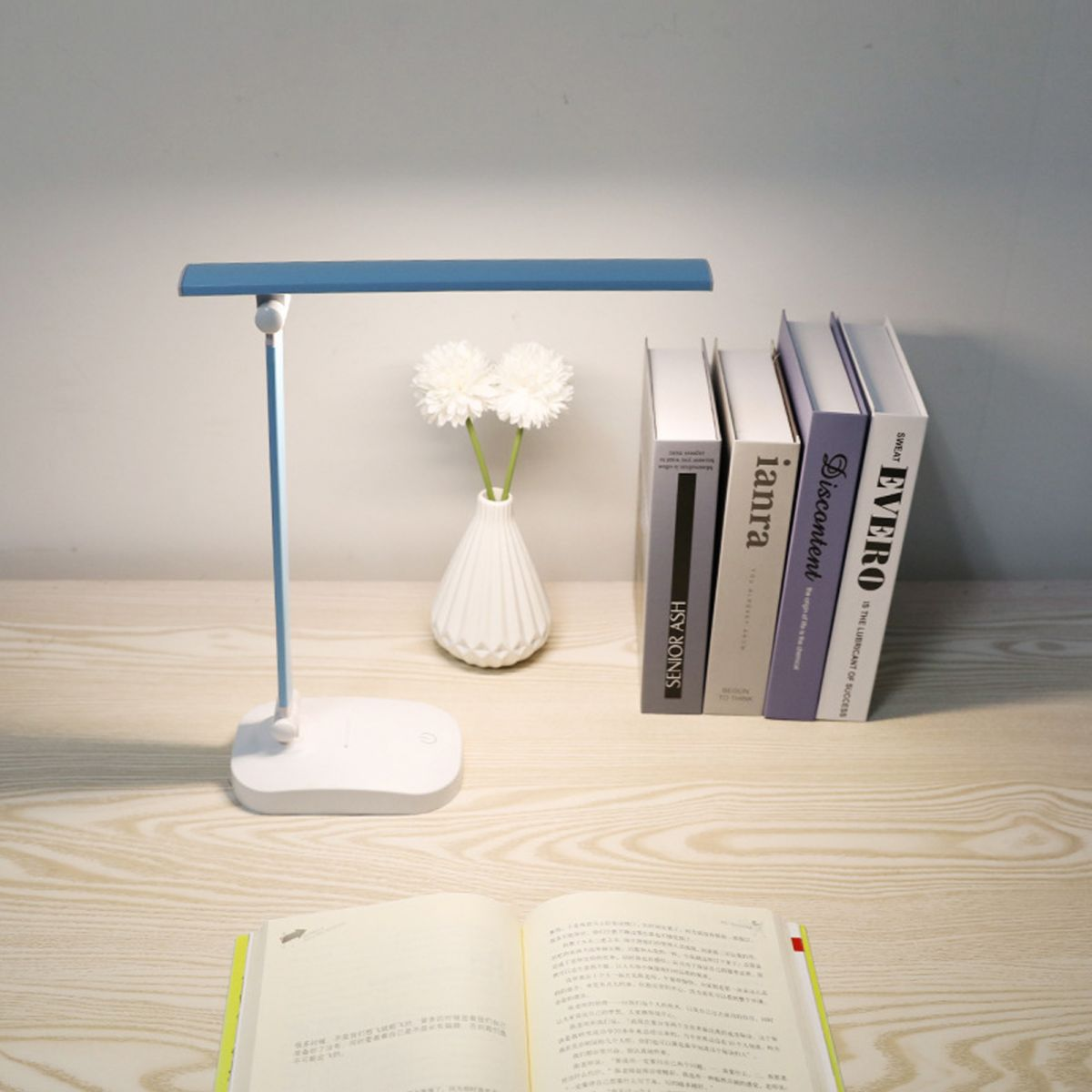 Ein blauer Schreibtischlampe steht neben Büchern und einer Vase mit Blumen.