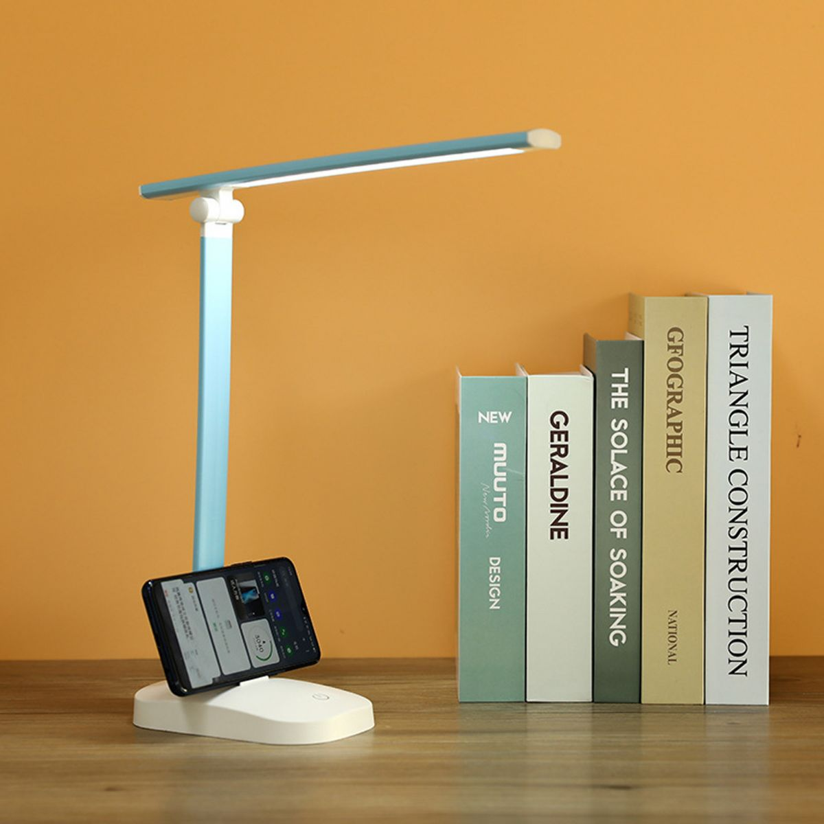 Eine blaue Schreibtischlampe mit beleuchtetem Stab, ein Smartphone und Bücher.