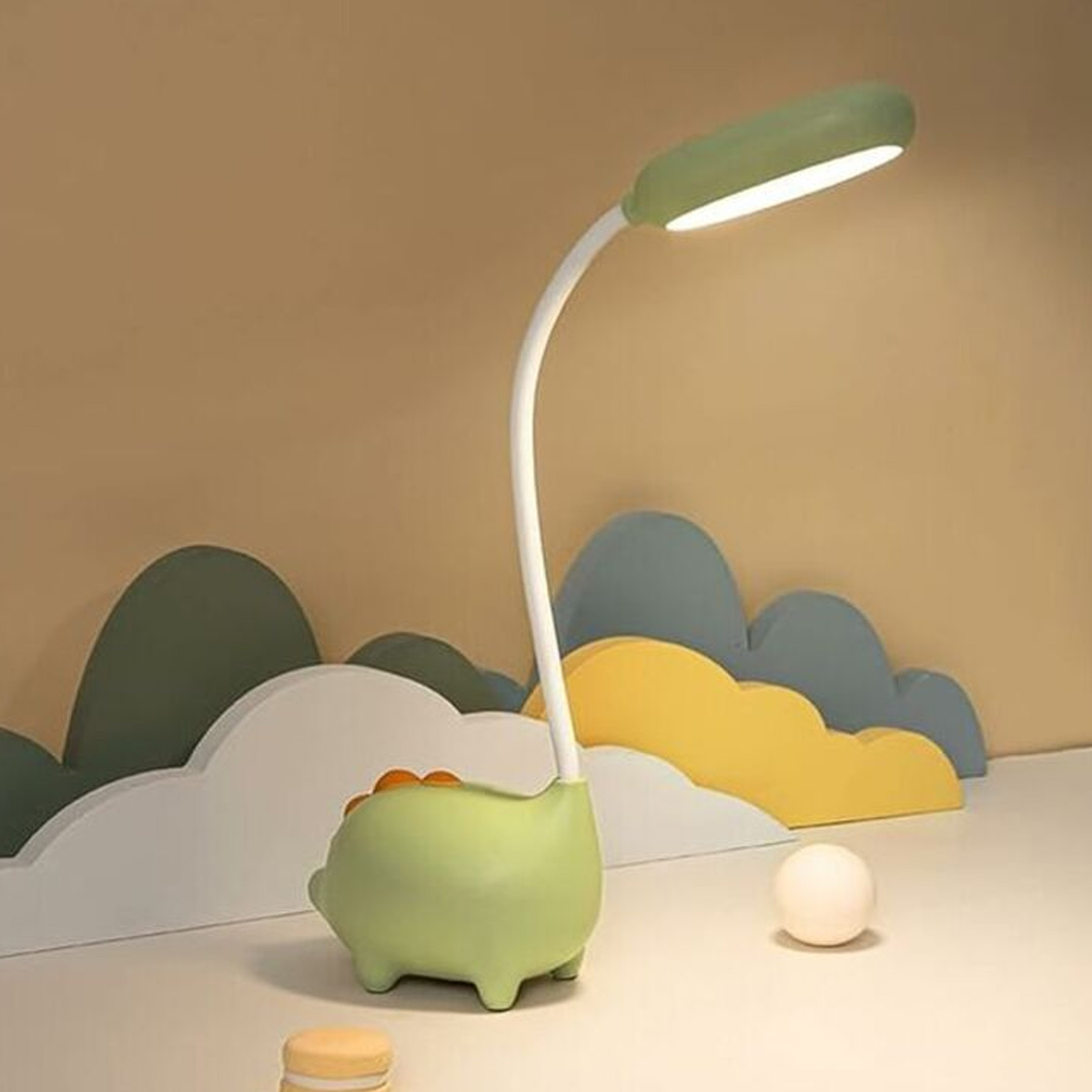 Eine grüne Dino-Lampe mit weißem Hals und einem hellen Licht, auf einem Schreibtisch.