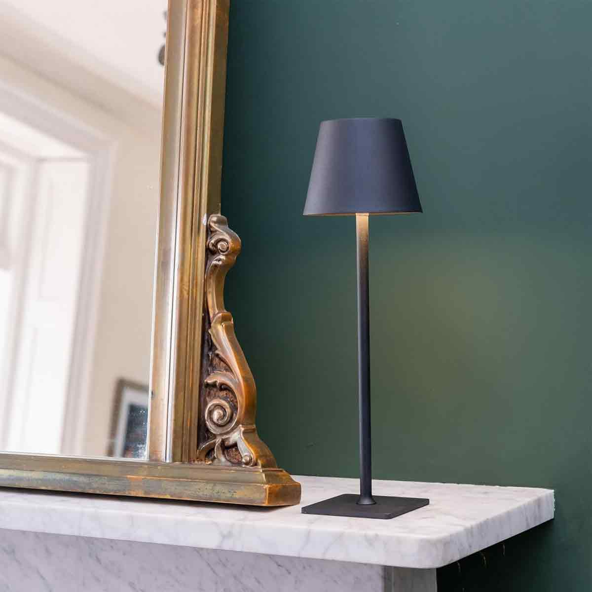 Ein schmaler Tisch mit Marmorplatte, ein Spiegel mit goldenem Rahmen und eine dunkle Lampe.