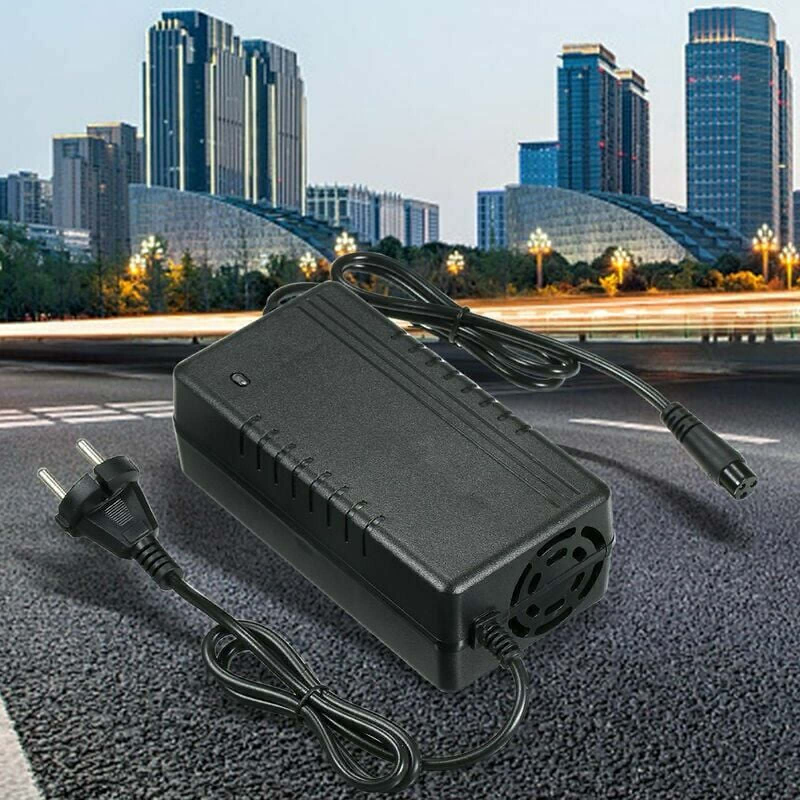 Schwarzes Ladegerät mit Kabel und Stecker auf Asphalt vor Stadtgebäuden.