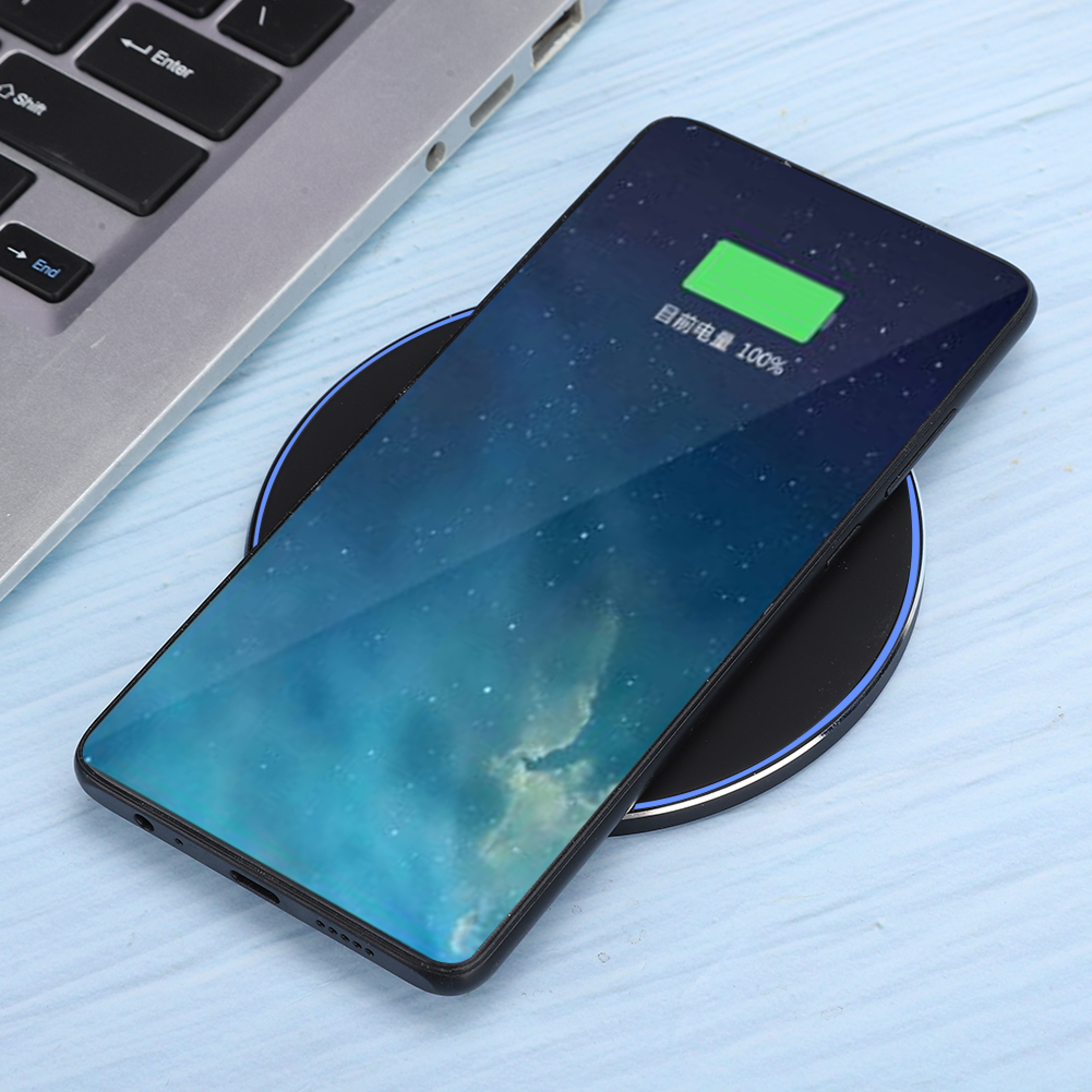 Ein Smartphone mit 100 % Akku liegt auf einer schwarzen Ladestation neben einer Tastatur.