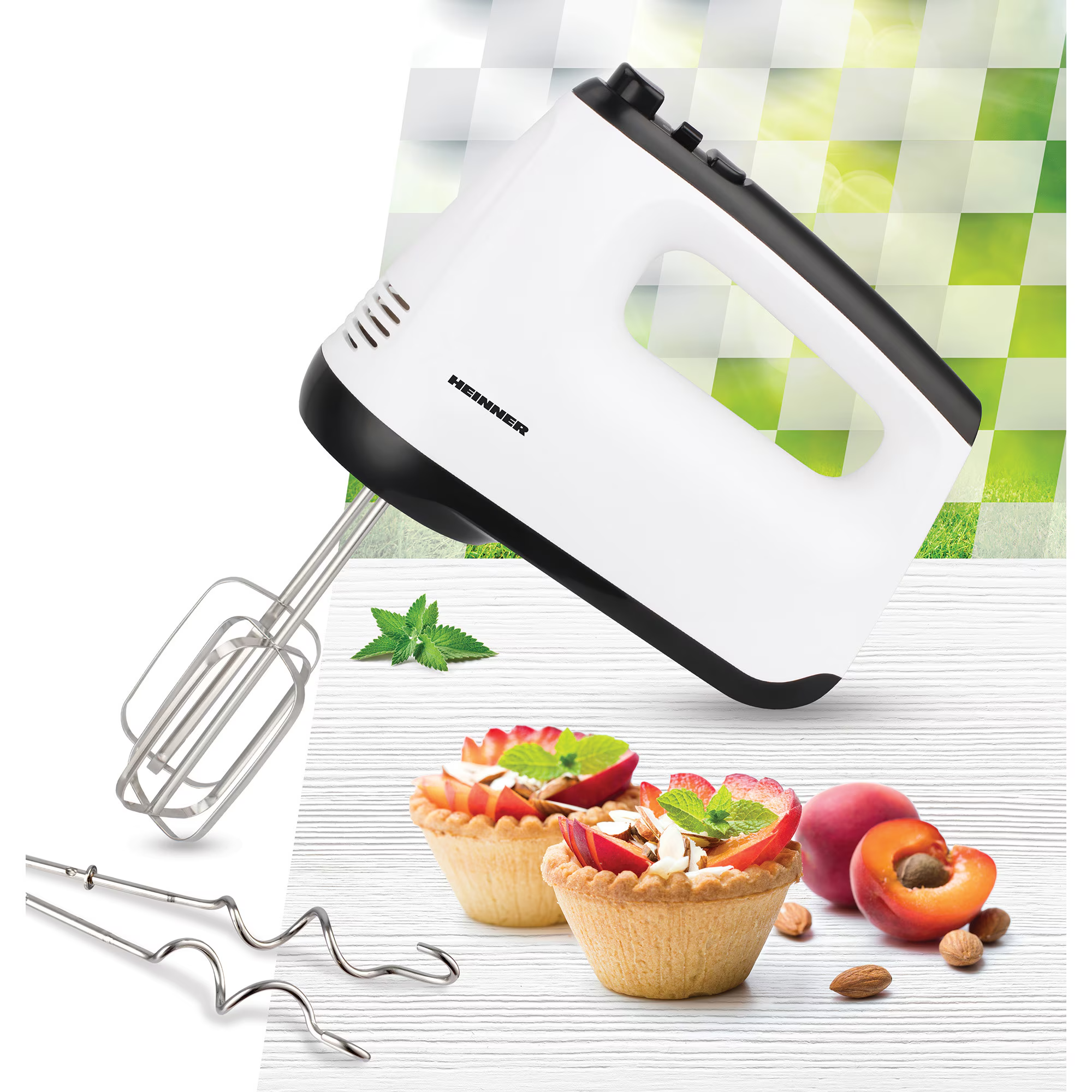 Een witte handmixer met zwarte accenten naast fruittaartjes en noten.
