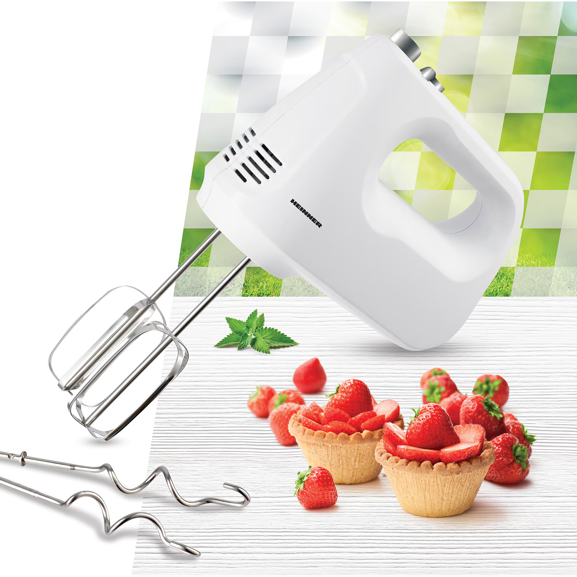 A white hand mixer with beaters and strawberry tarts on a wooden table.